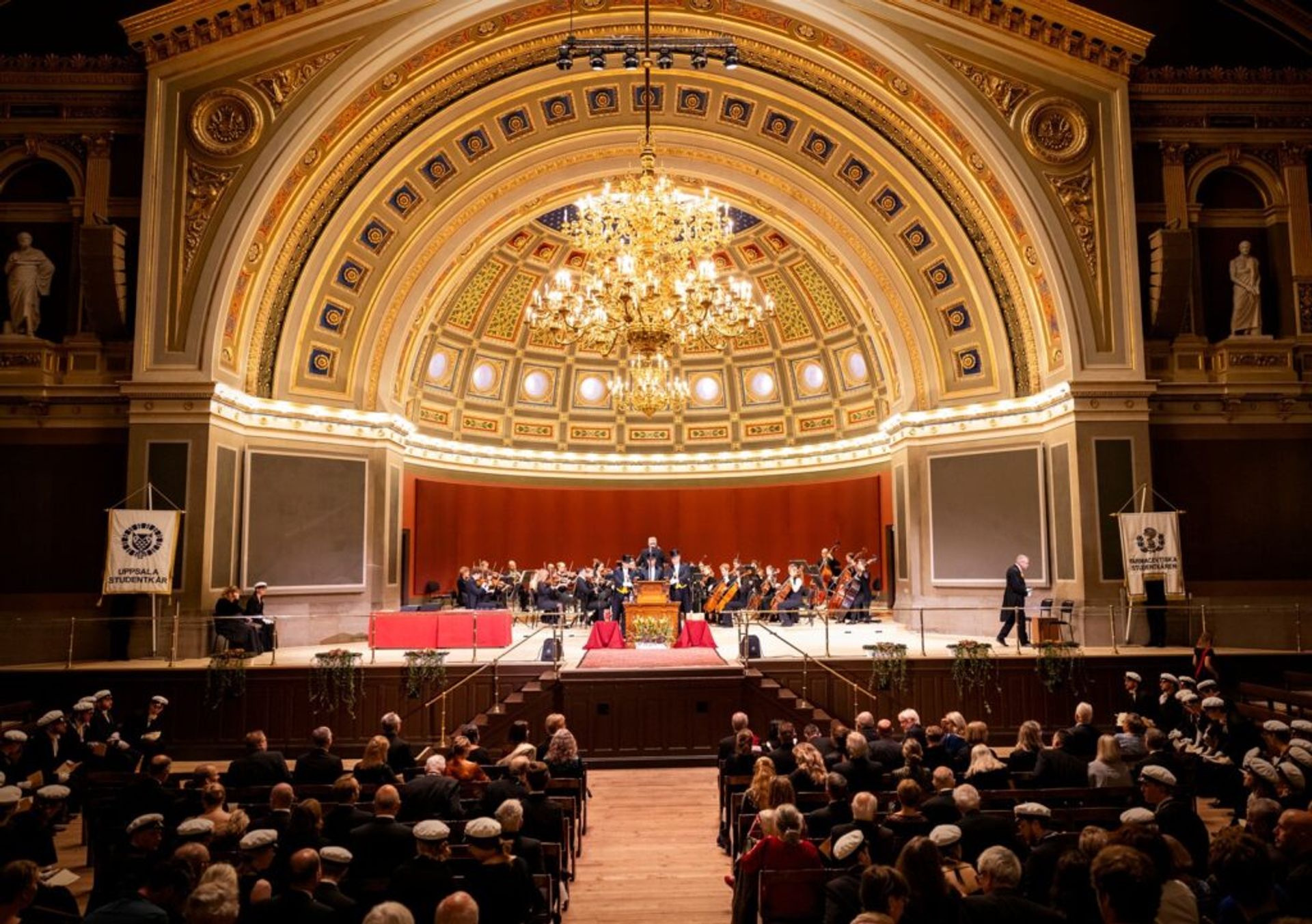 An orchestra playing on a stage inside the autitorium of Uppsala University's Main Building.