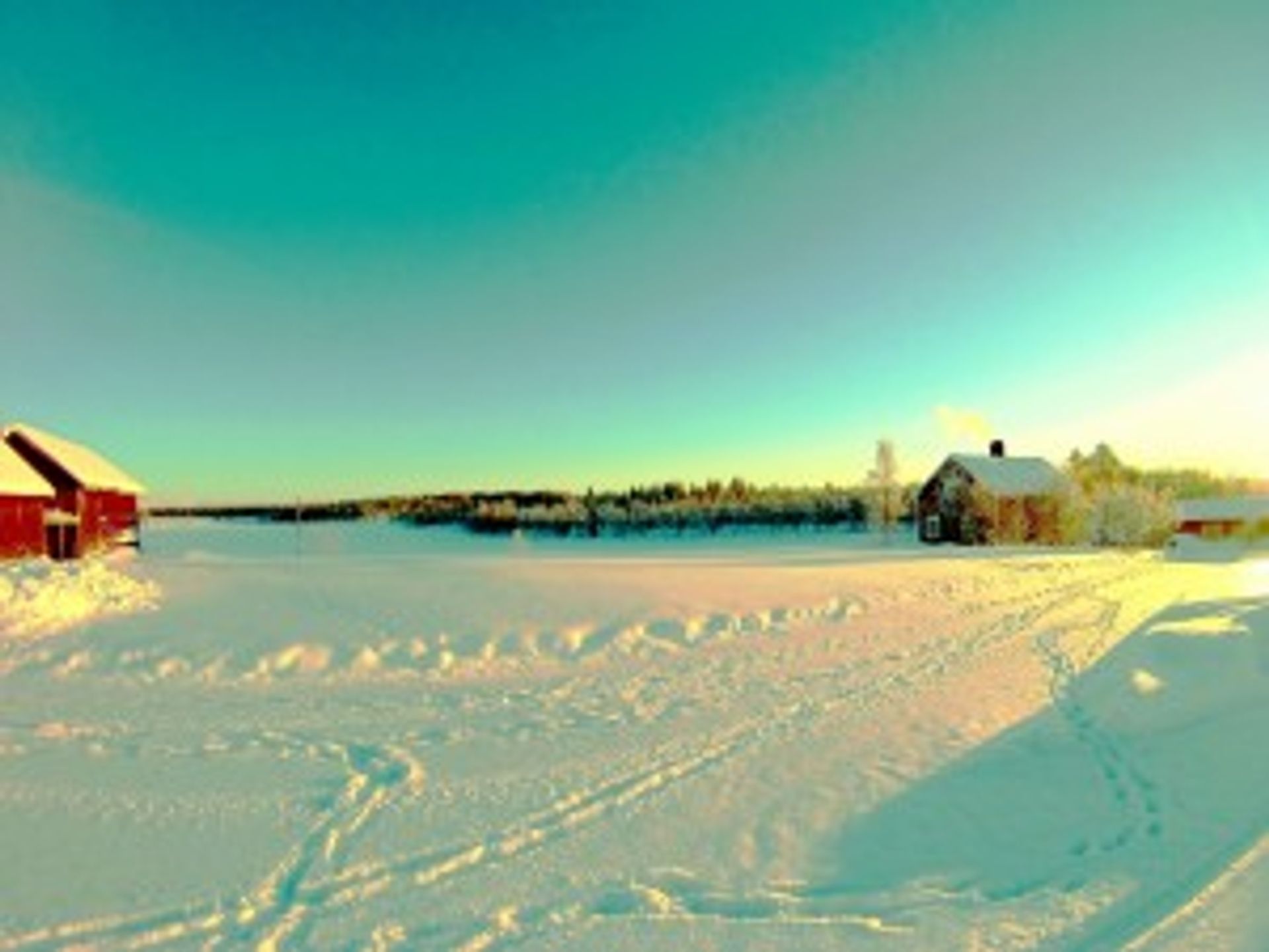 A landscape picture where the white snow takes up most of the picture and two red cottages are visible. The sun is shining and it is a green sky