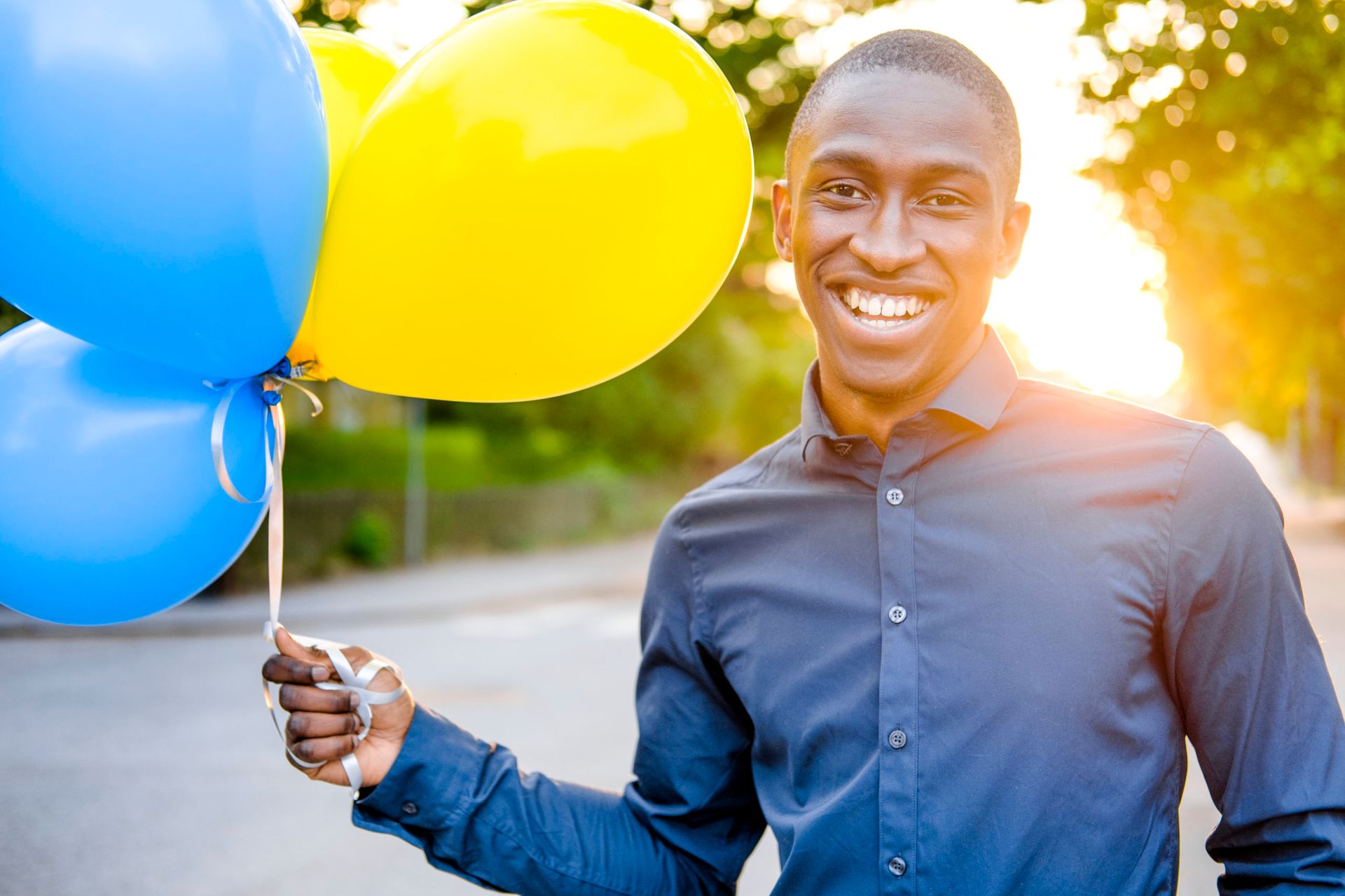 A male student holding balloons with the colors yellow and blue at the same time as he smiles into the camera.