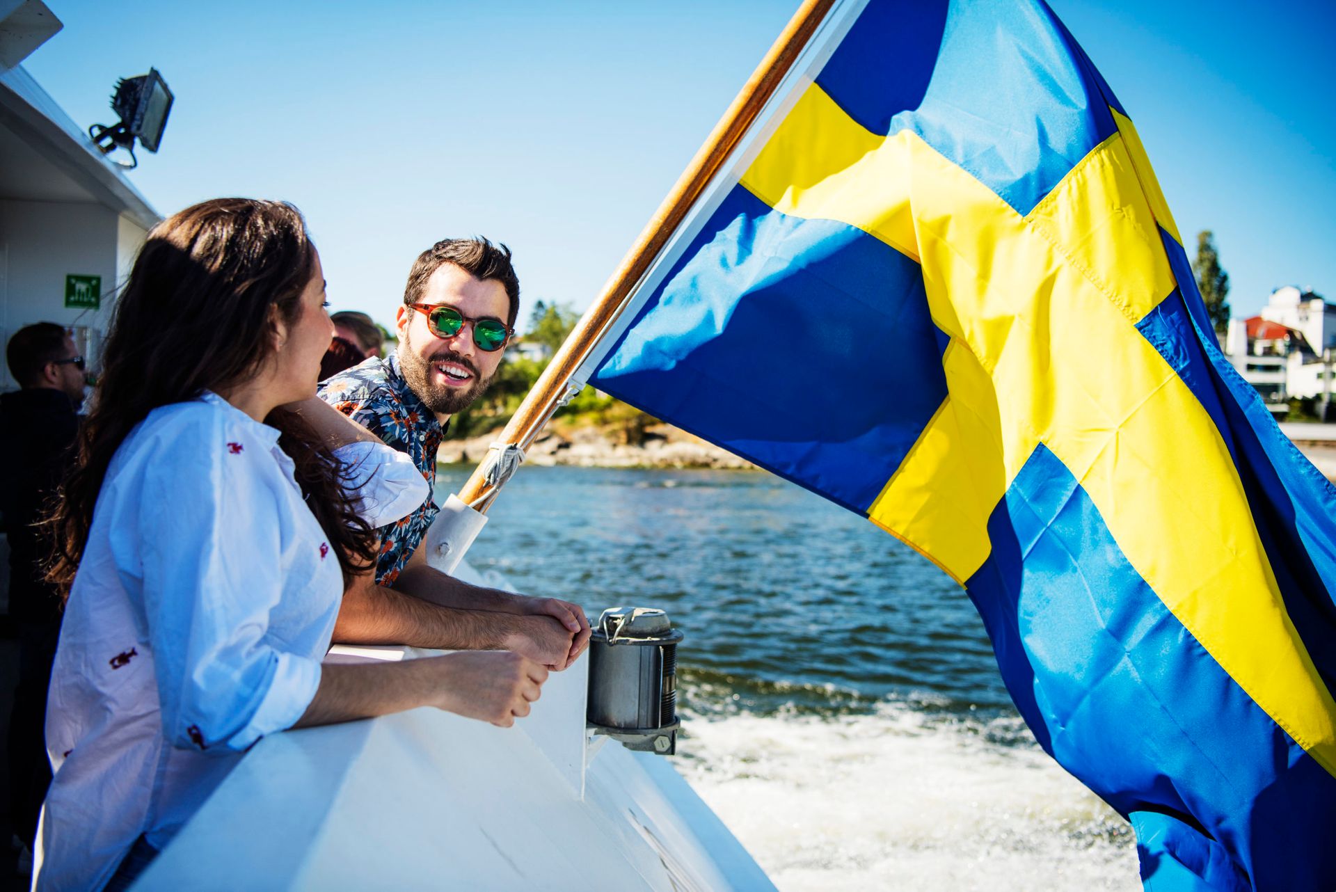 Friends by the water during summer time on a boat ride with the Swedish flag.