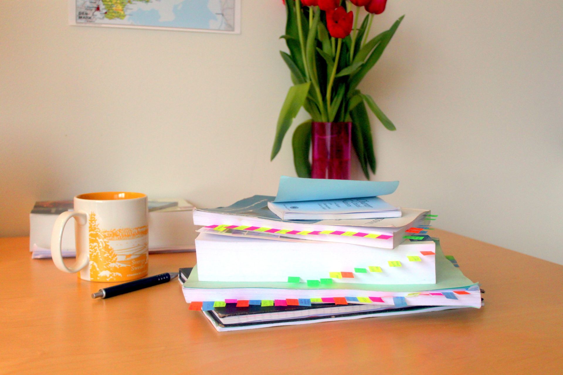 Coursebooks on a table. The books are full of multi-coloured stickynotes.