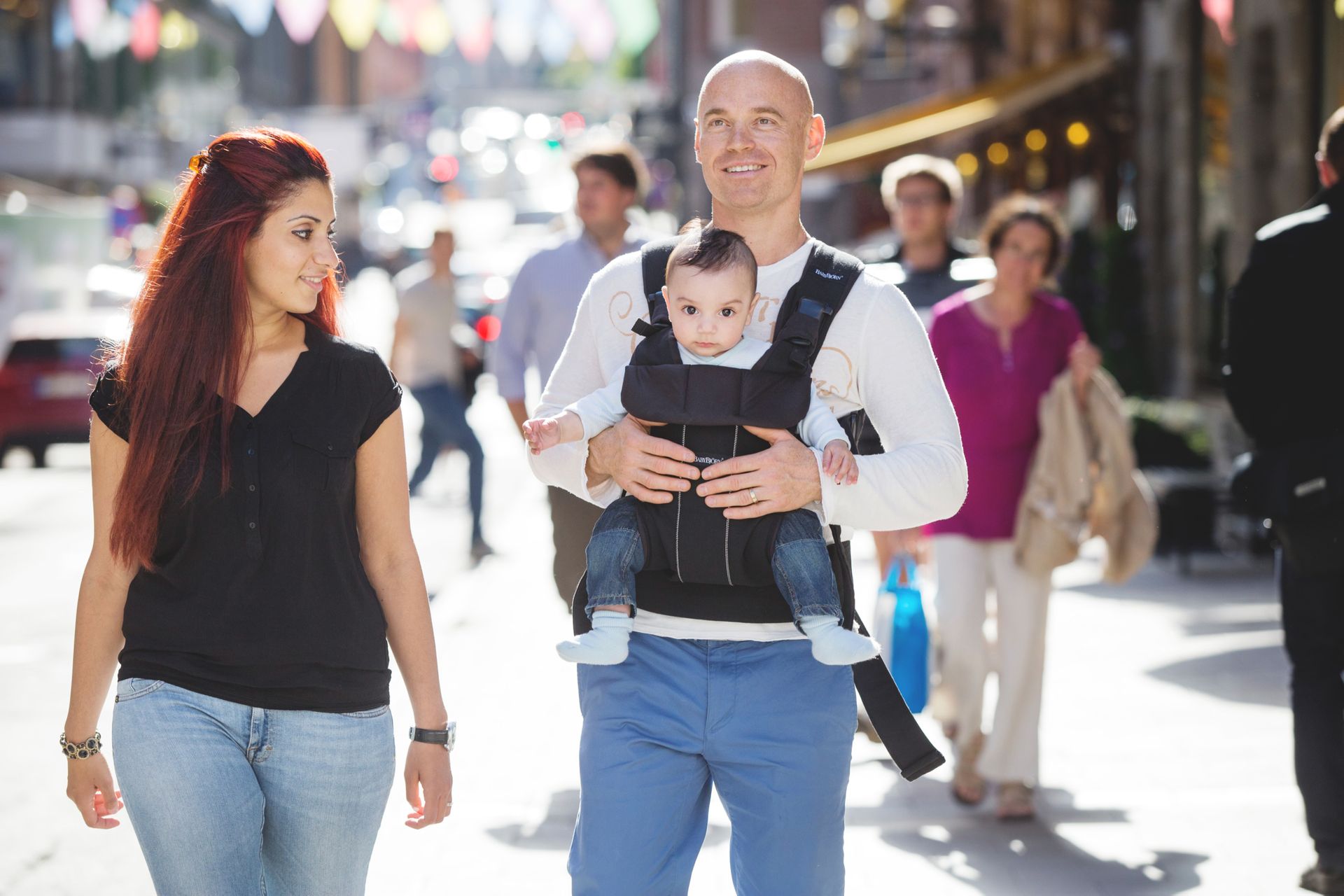 Two people walking down a street. One person is carrying a baby in a baby sling.