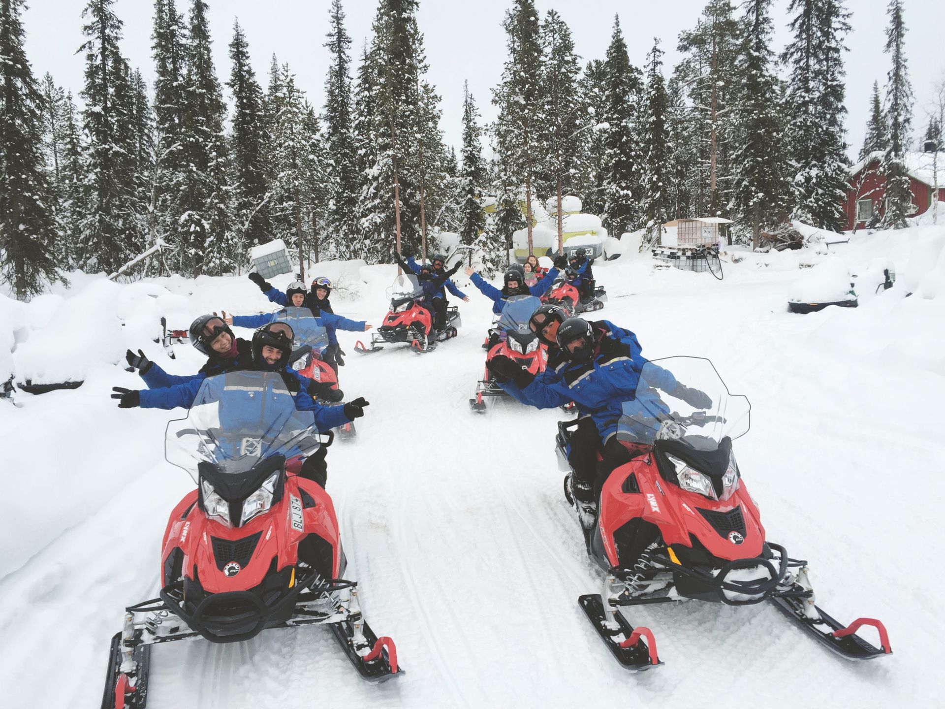 A group of people on snowmobiles, lined up on a snowy trail surrounded by forest.
