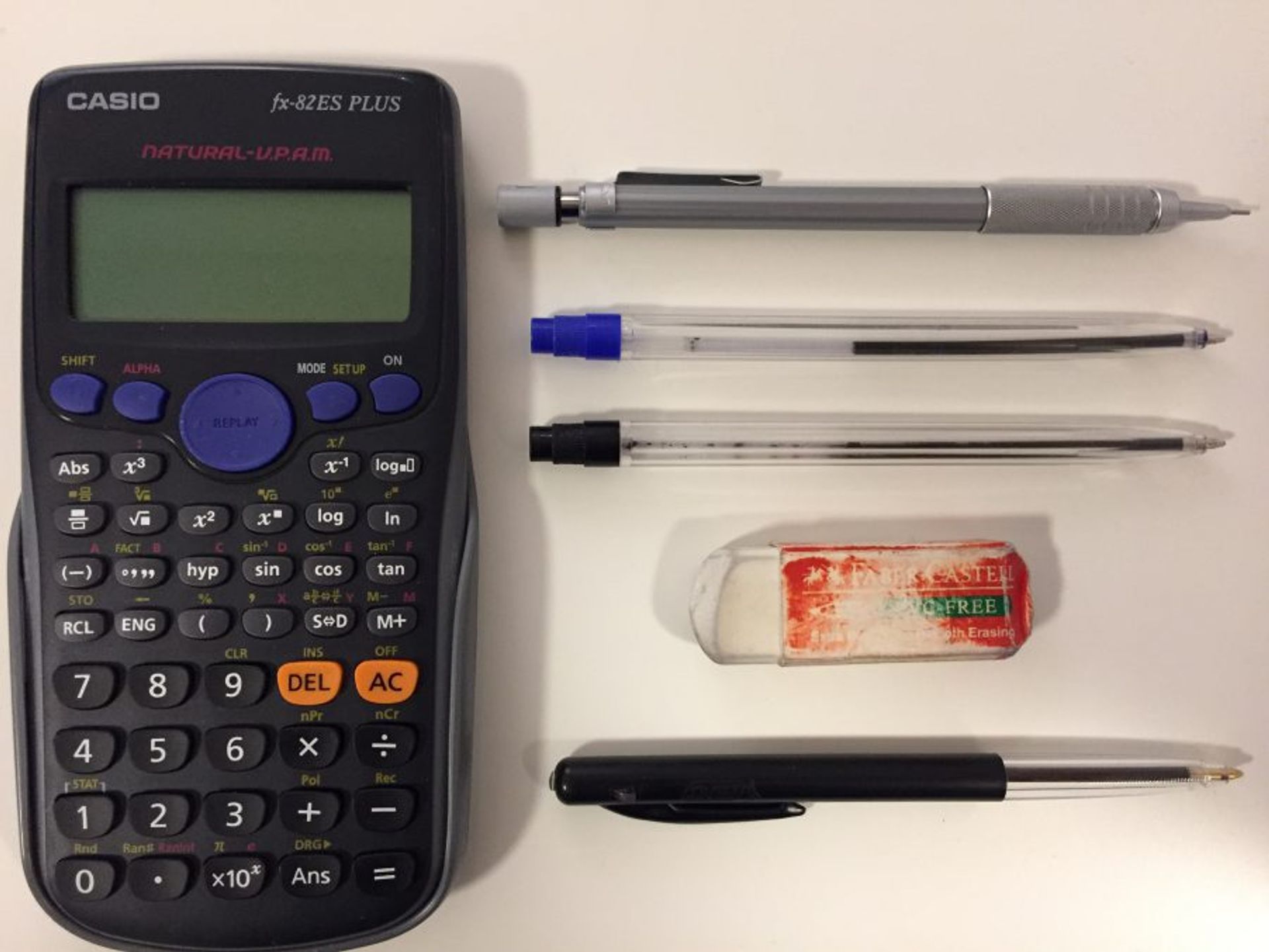 Four pens, an eraser and a calculator on a table.