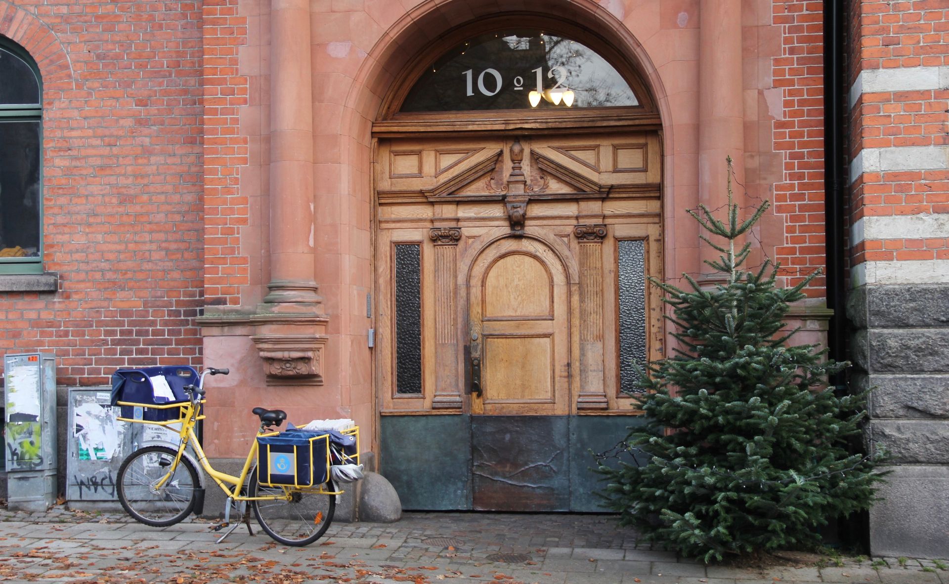 A yellow bicycle used by the postal service parked outside of a building.