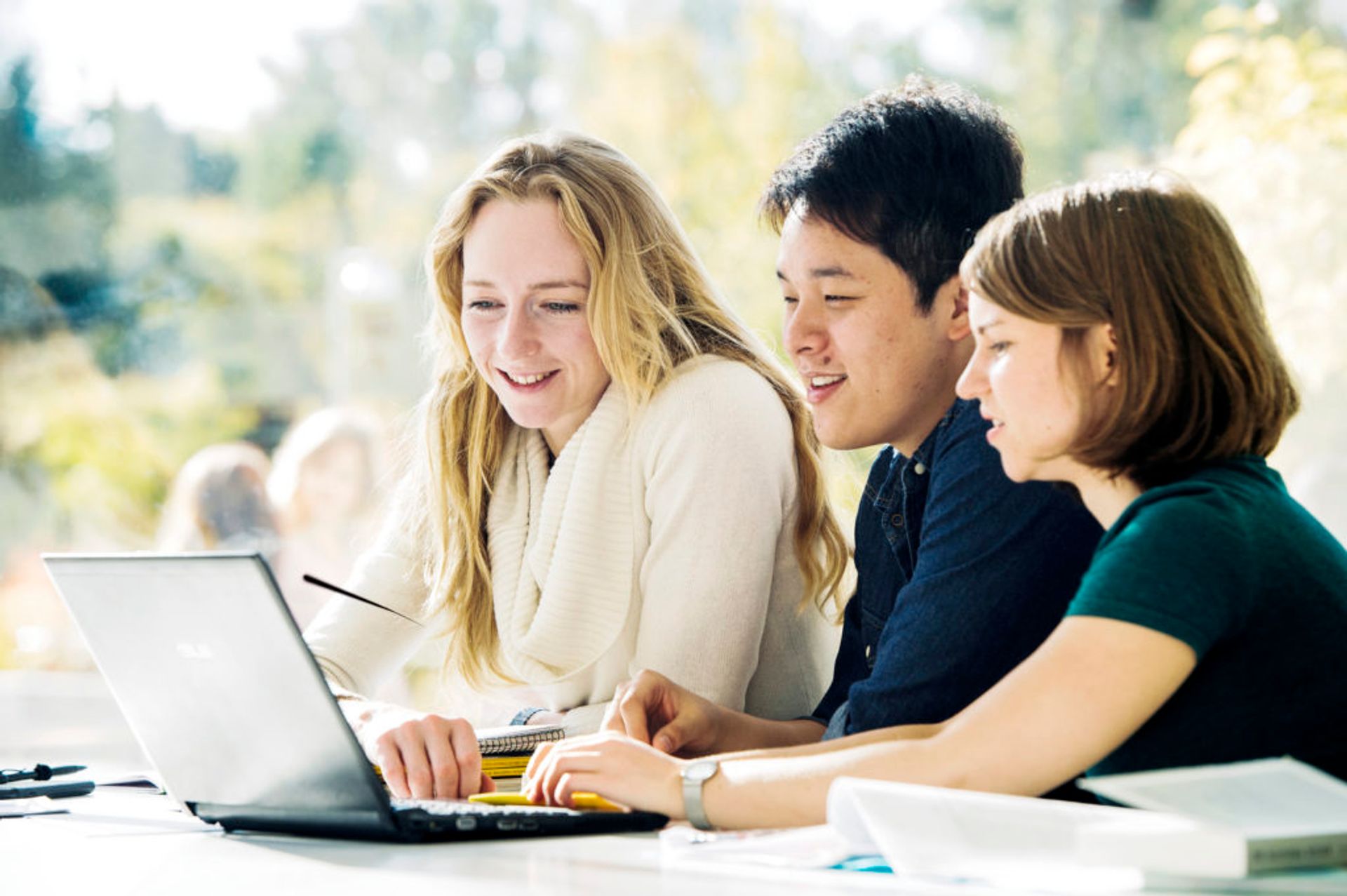 Three international students look at a laptop while working on a group project.