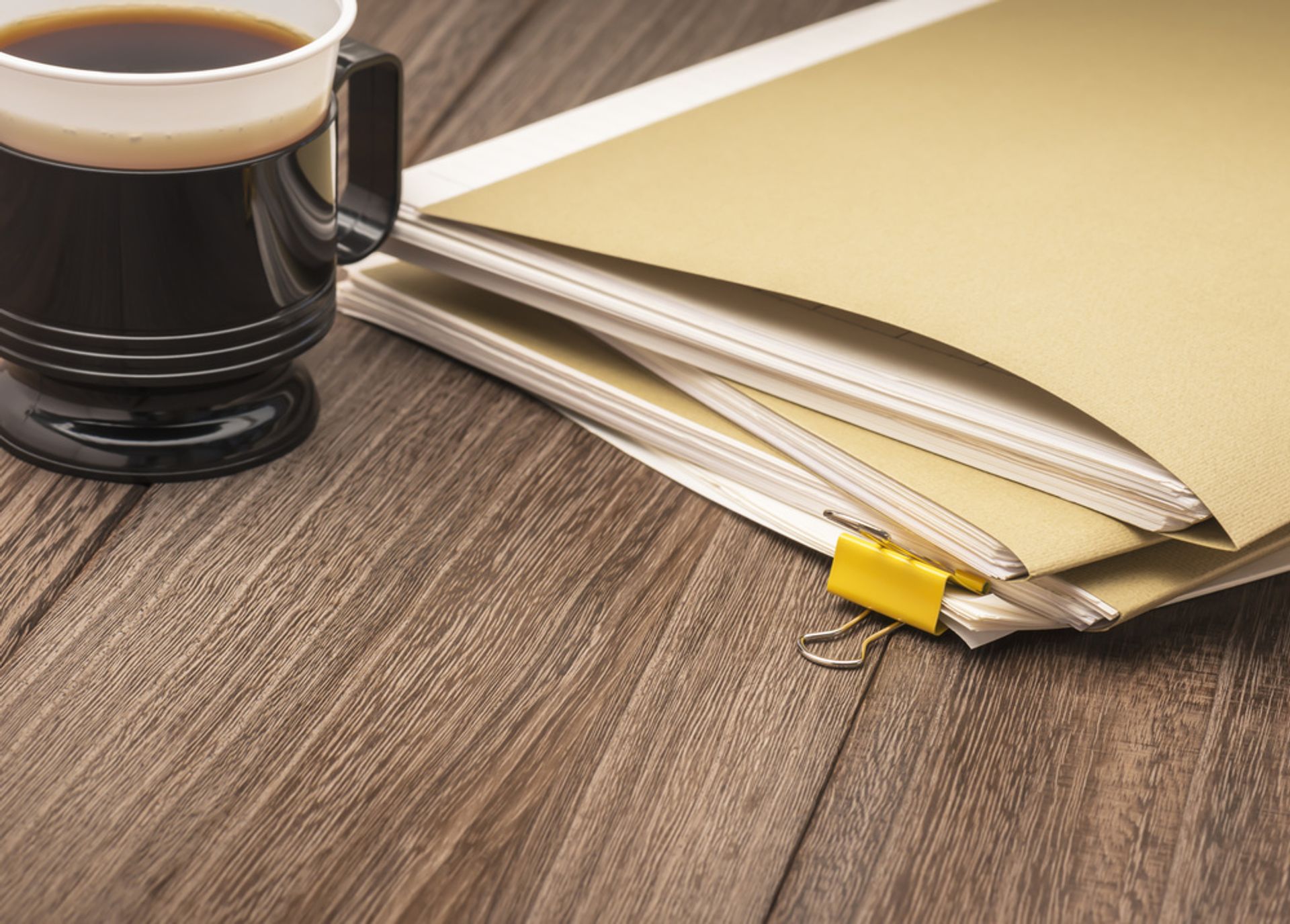 A pile of document files set beside a cup of coffee.