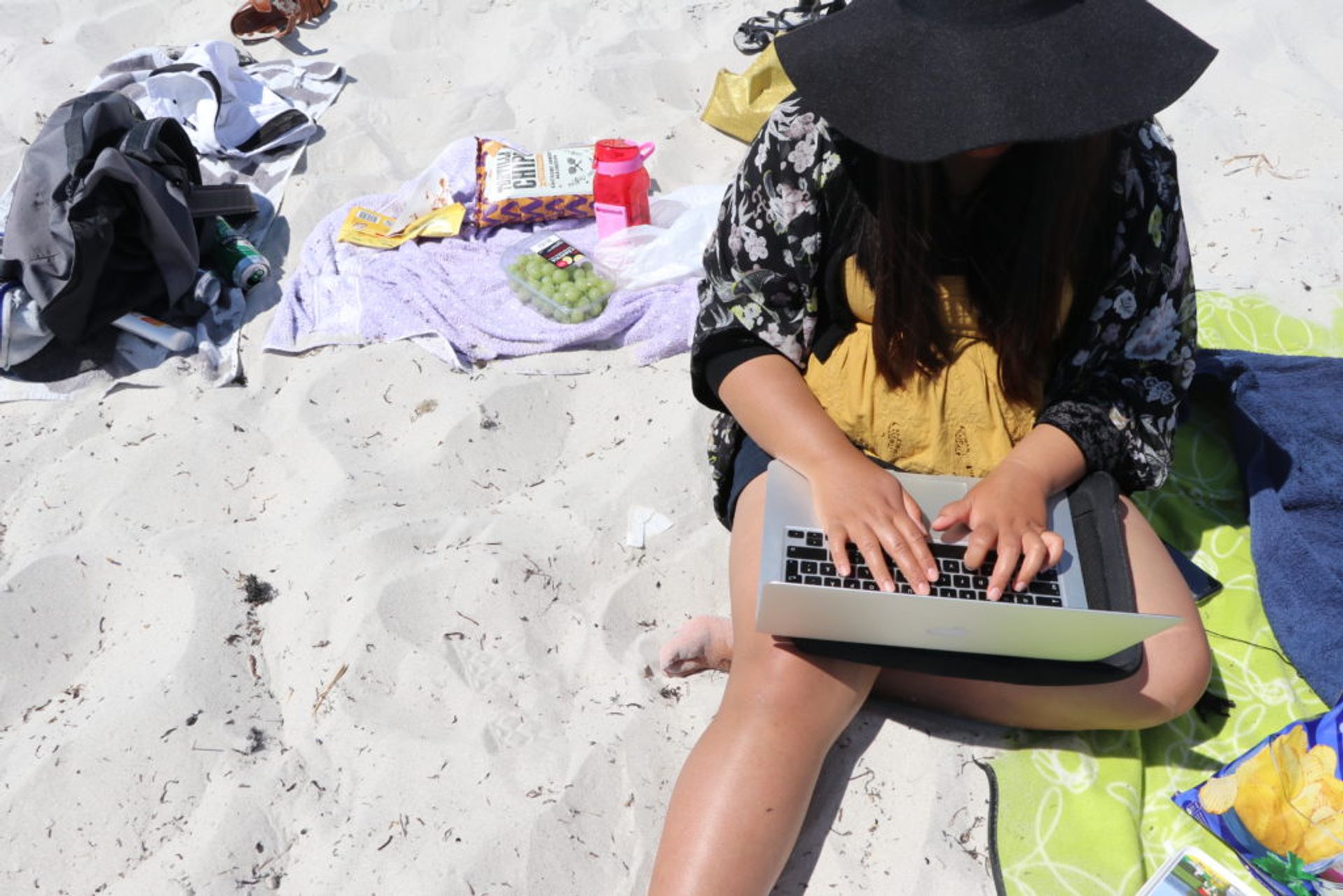 A person sits on the beach typing on a laptop.