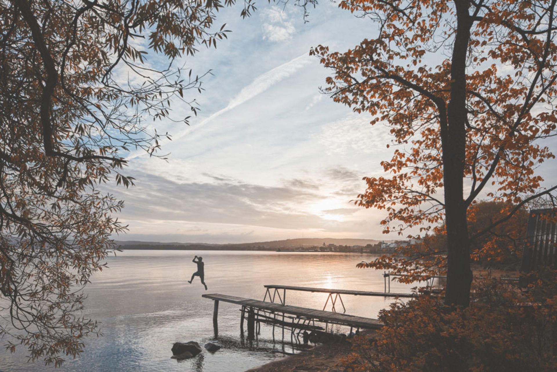 Person jumping off a wooden jetty into a lake.