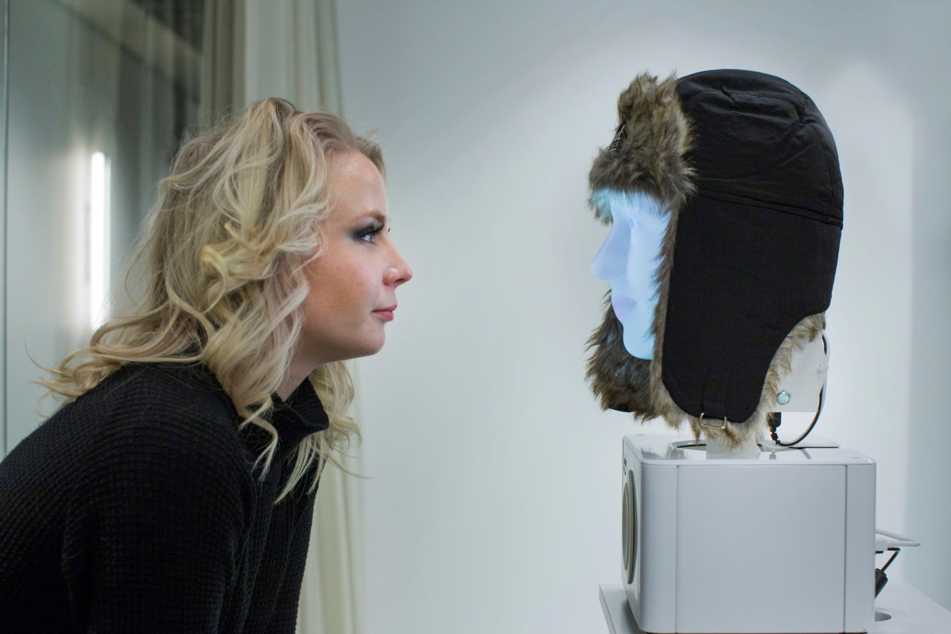 A woman examines a mannequin head wearing a winter hat.