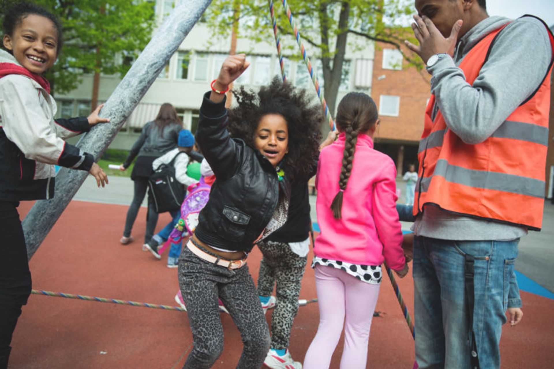 A child goofing around at the playground. The other children around are smiling and so does the teacher watching.