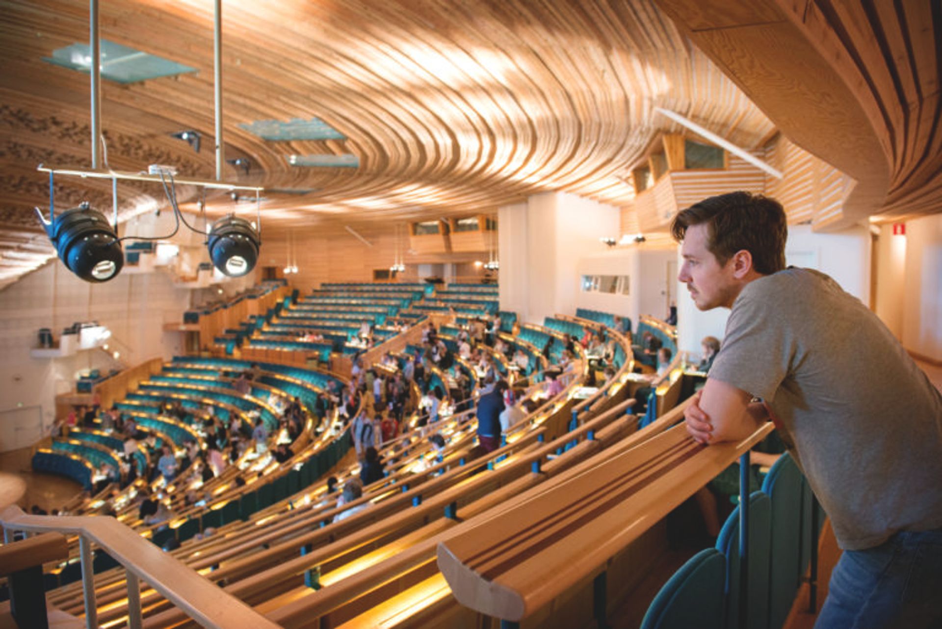 A man at the top of a big assembly hall, looking down on people having their seats.