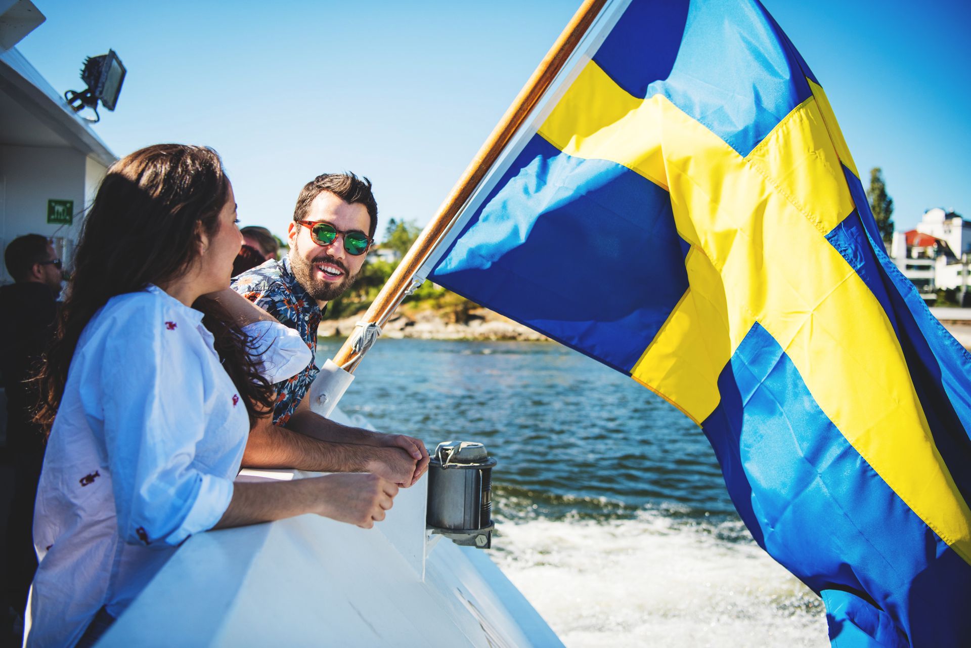 Two people standing beside the Swedish flag at the back of a boat.