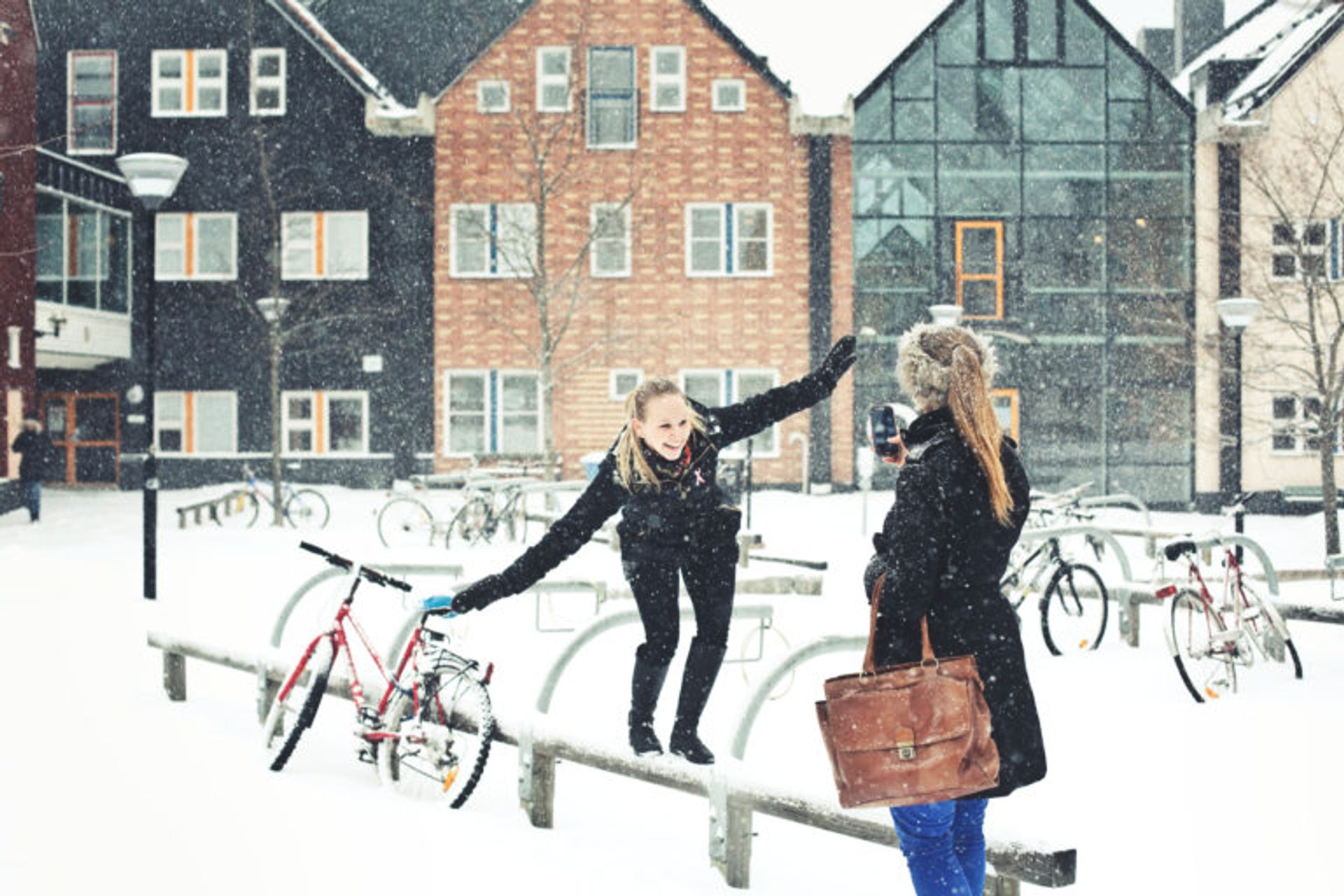 A woman who is balancing on a wooden railing. It is sowing and her friend is waiting for her.