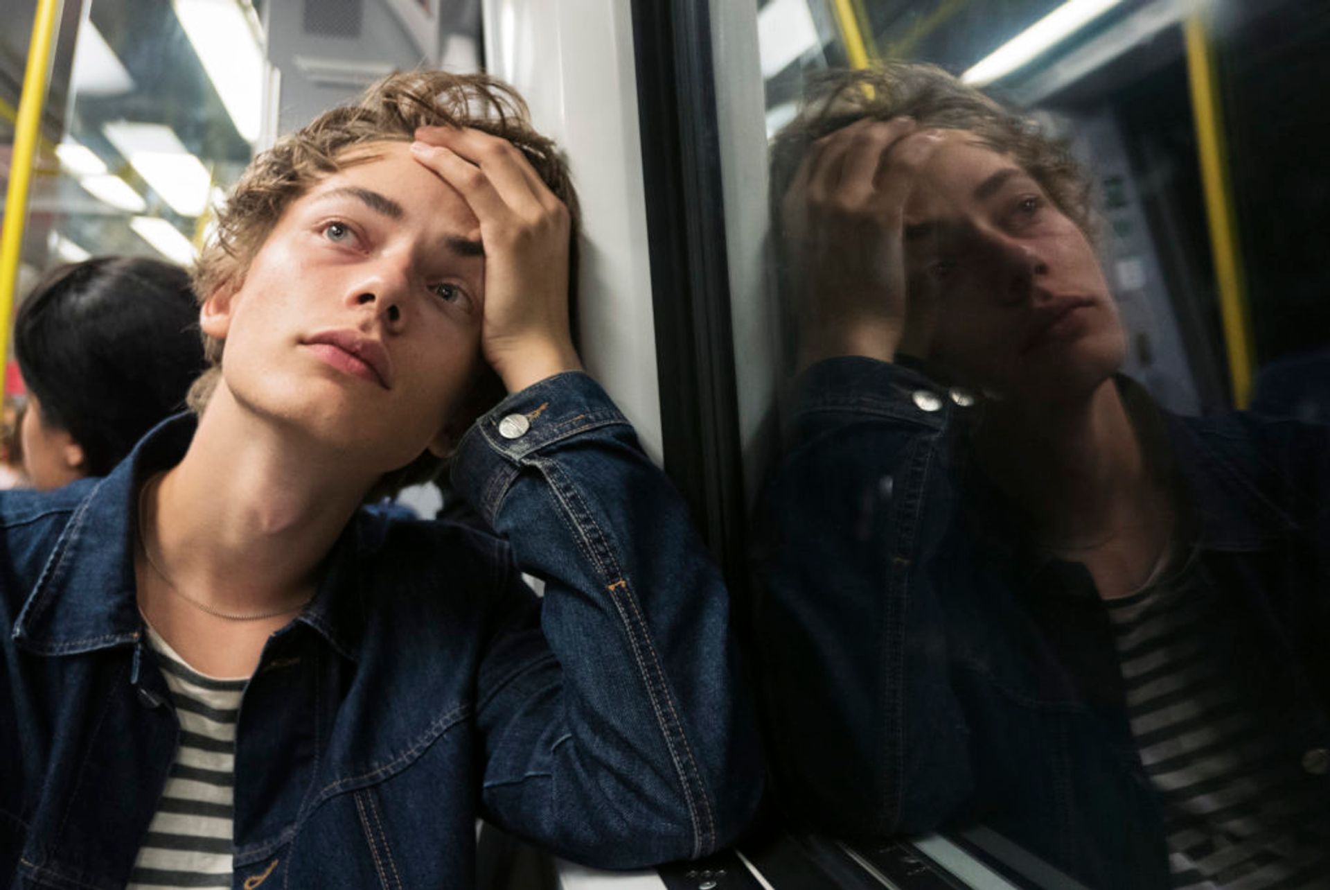 A young man on the subway holding his forehead in his palm like something is bothering him.