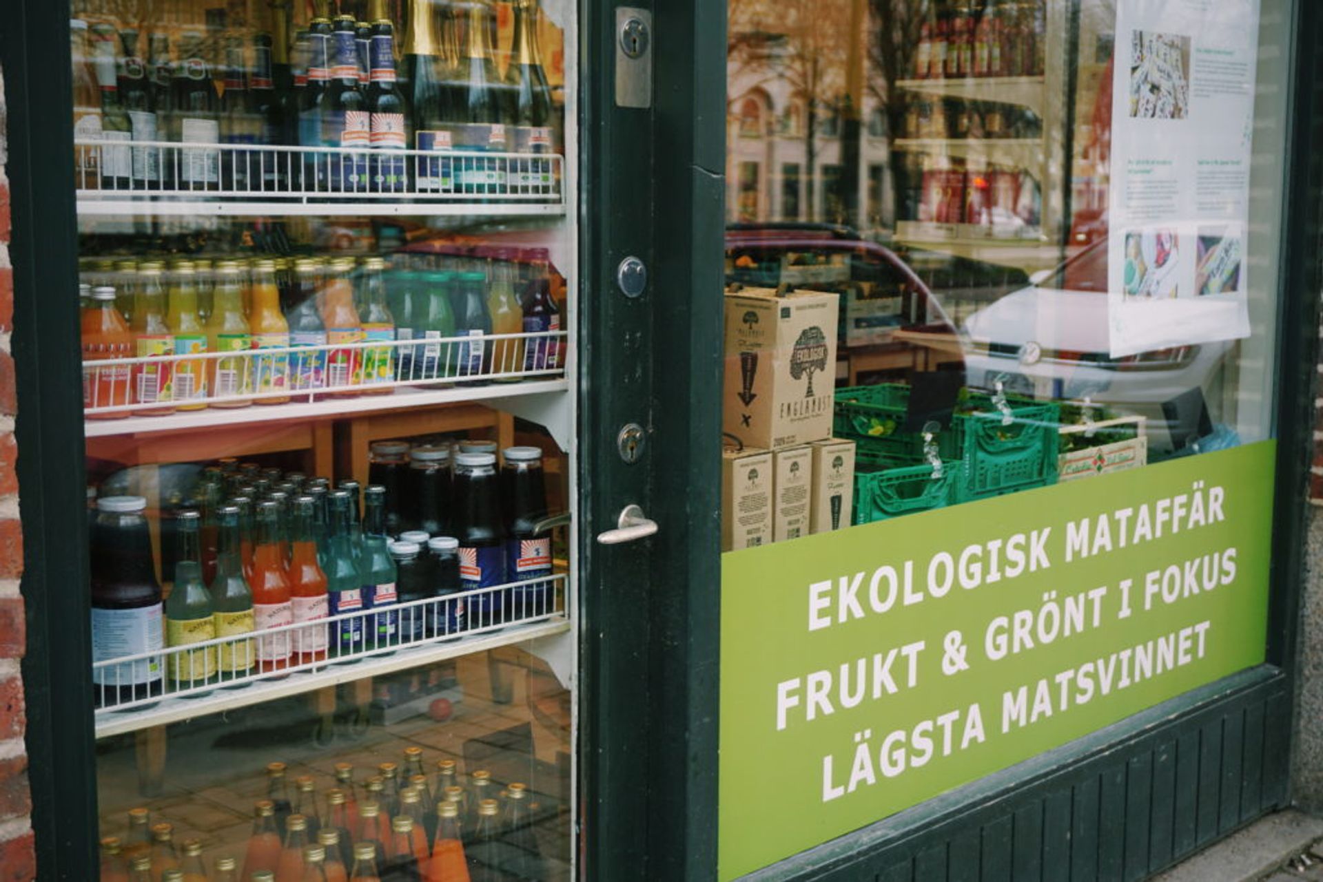 A window of an ecological store in Sweden. You can see bottle, cans and and a sign saying the store has fruit and greens in focus. 
