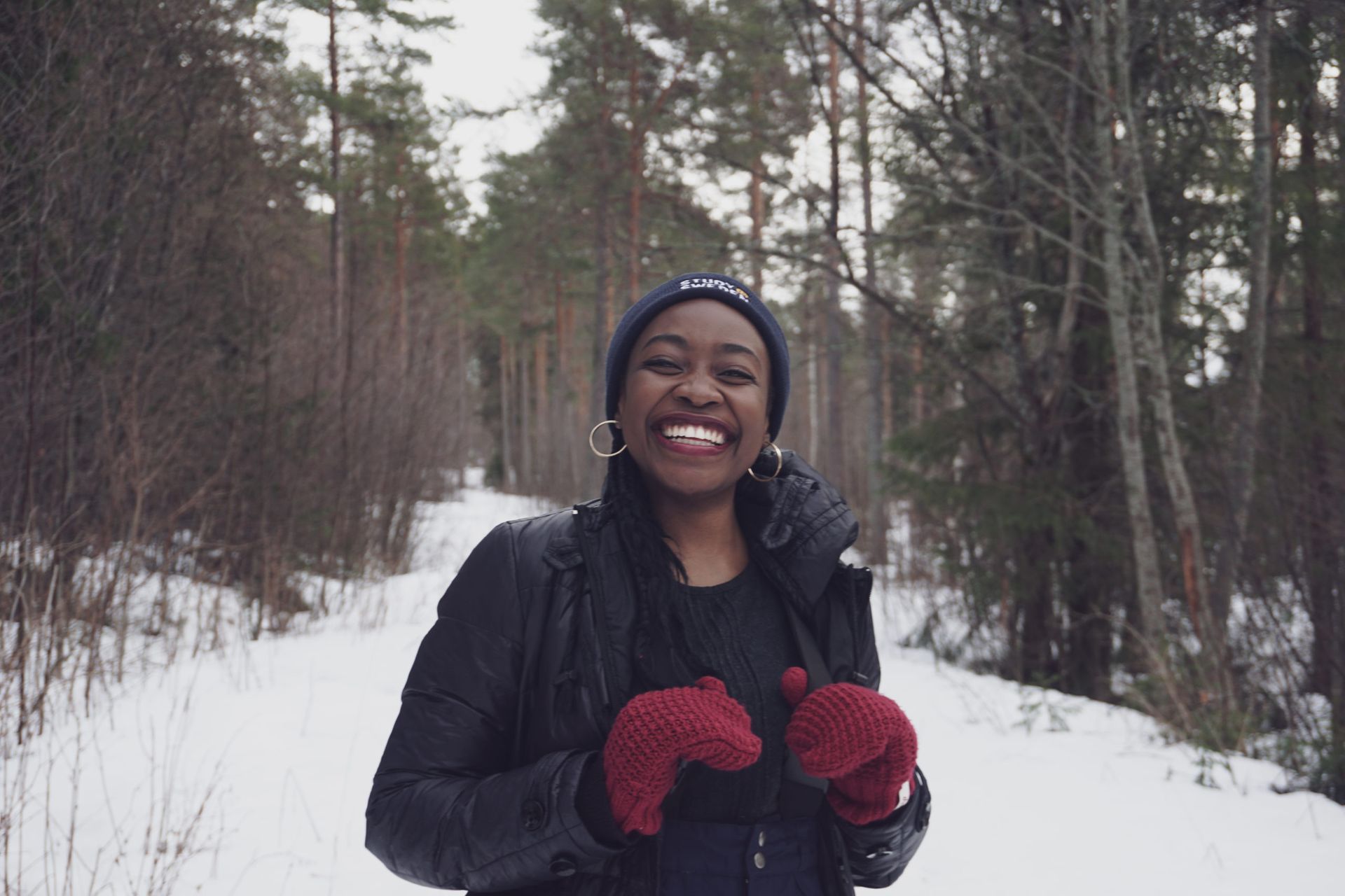 A smiling woman on a snowy, yet cloudy, day in the woods.