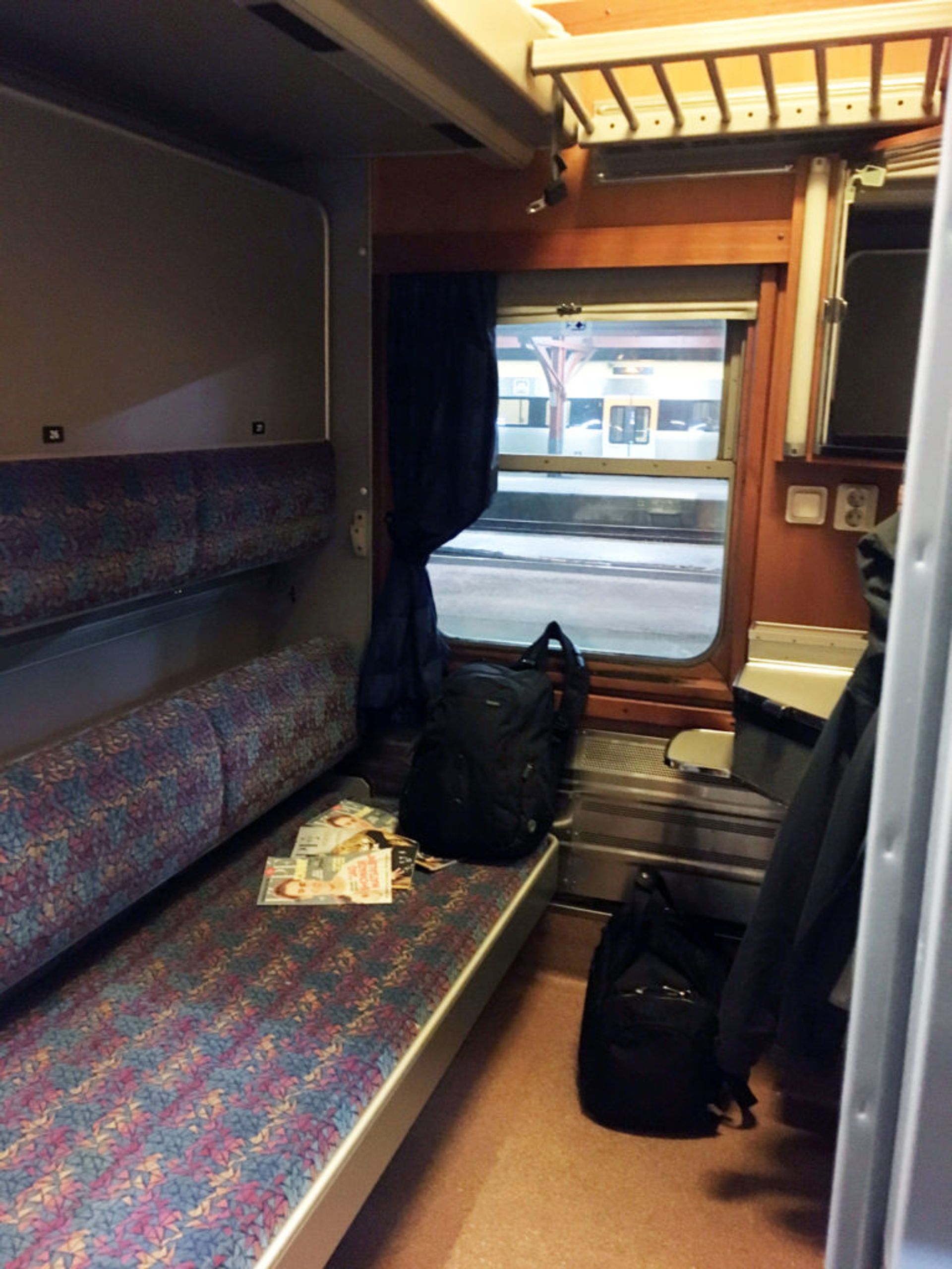 Small cabin at a sleeper train. You can see a colourful seat, a small table and a small window. 