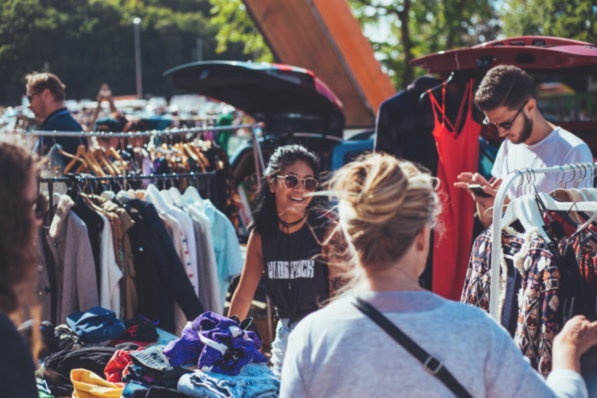 A smiling girl at a stand on a flea market, surrounded by clothes, on a sunny summer day.