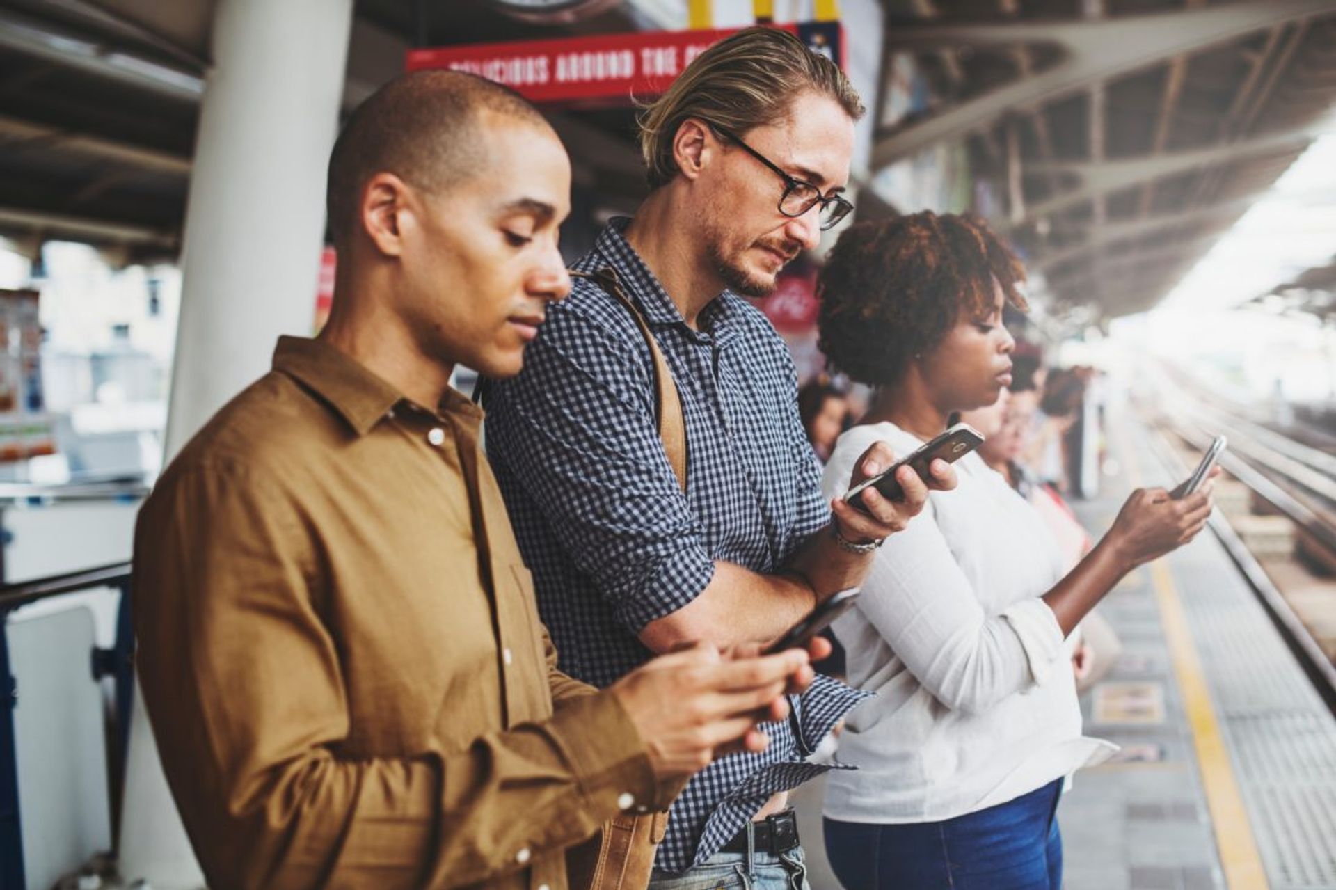 People looking at their mobile phones at a train station.