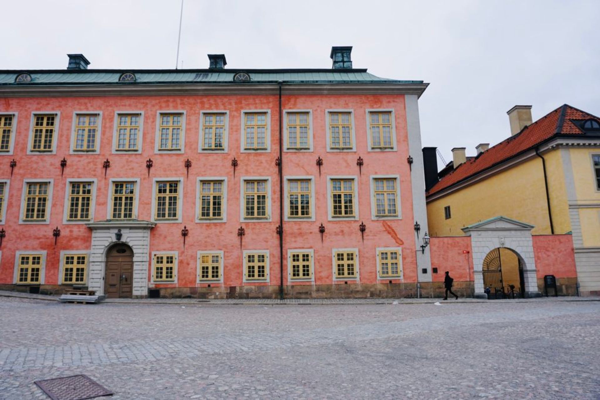 A woman walking past a large pink building.