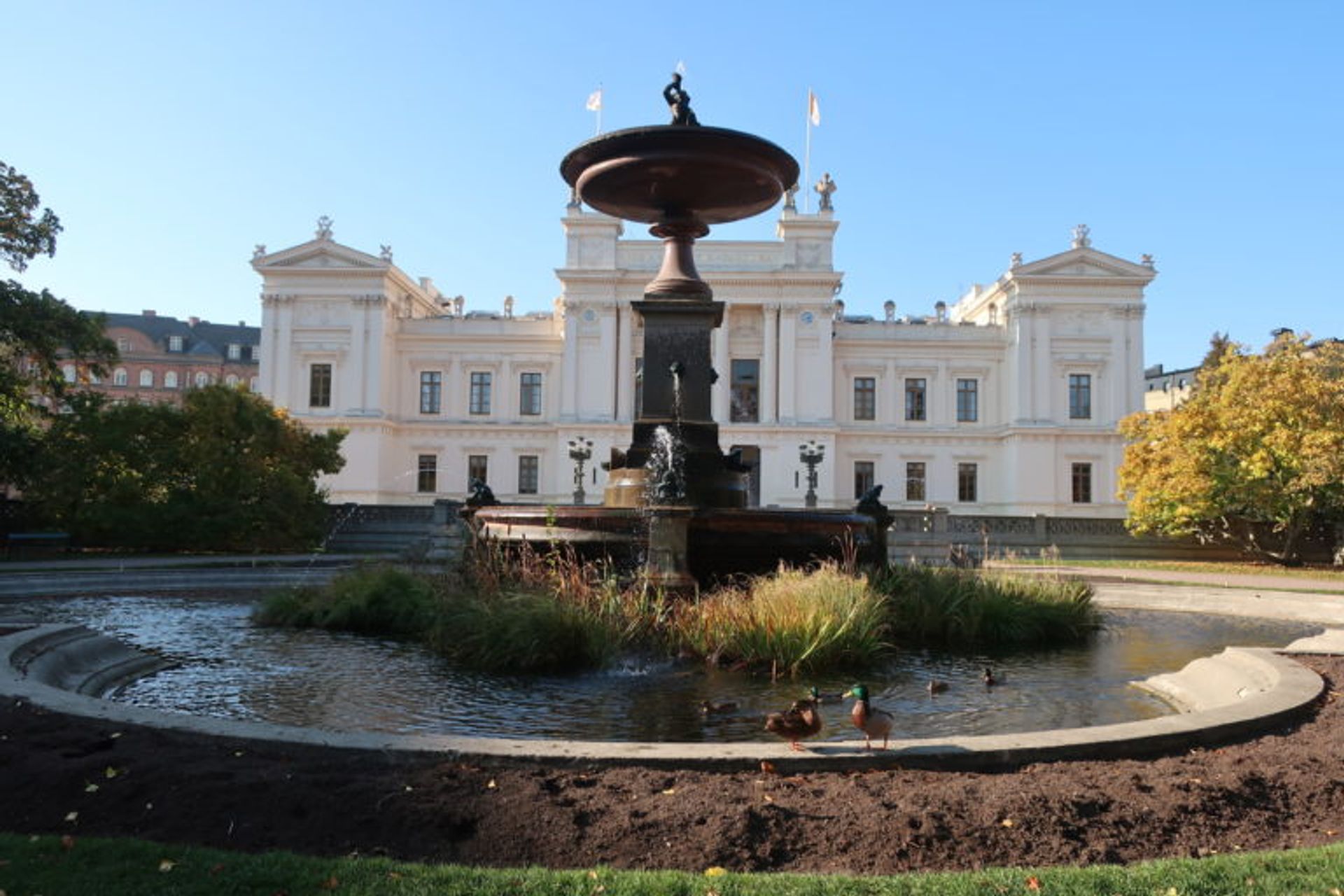 In front of Lund University. A big white building with a water fountain right in front of the stair entrance.