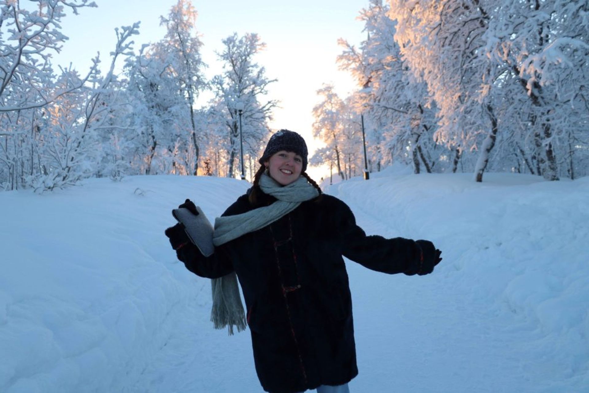 A woman on a really snowy day. It is all white, she is smiling and the sun is shining.
