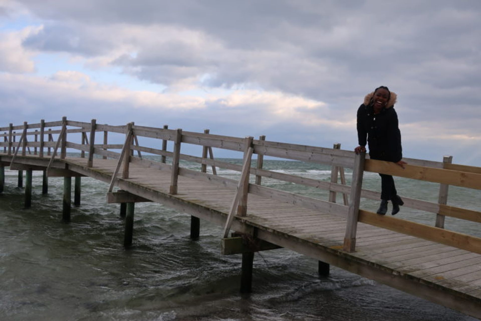 The Author Concillier is at a jetty, smiling. It is a cloudy day in spring, Concillier is wearing a winter jacket.