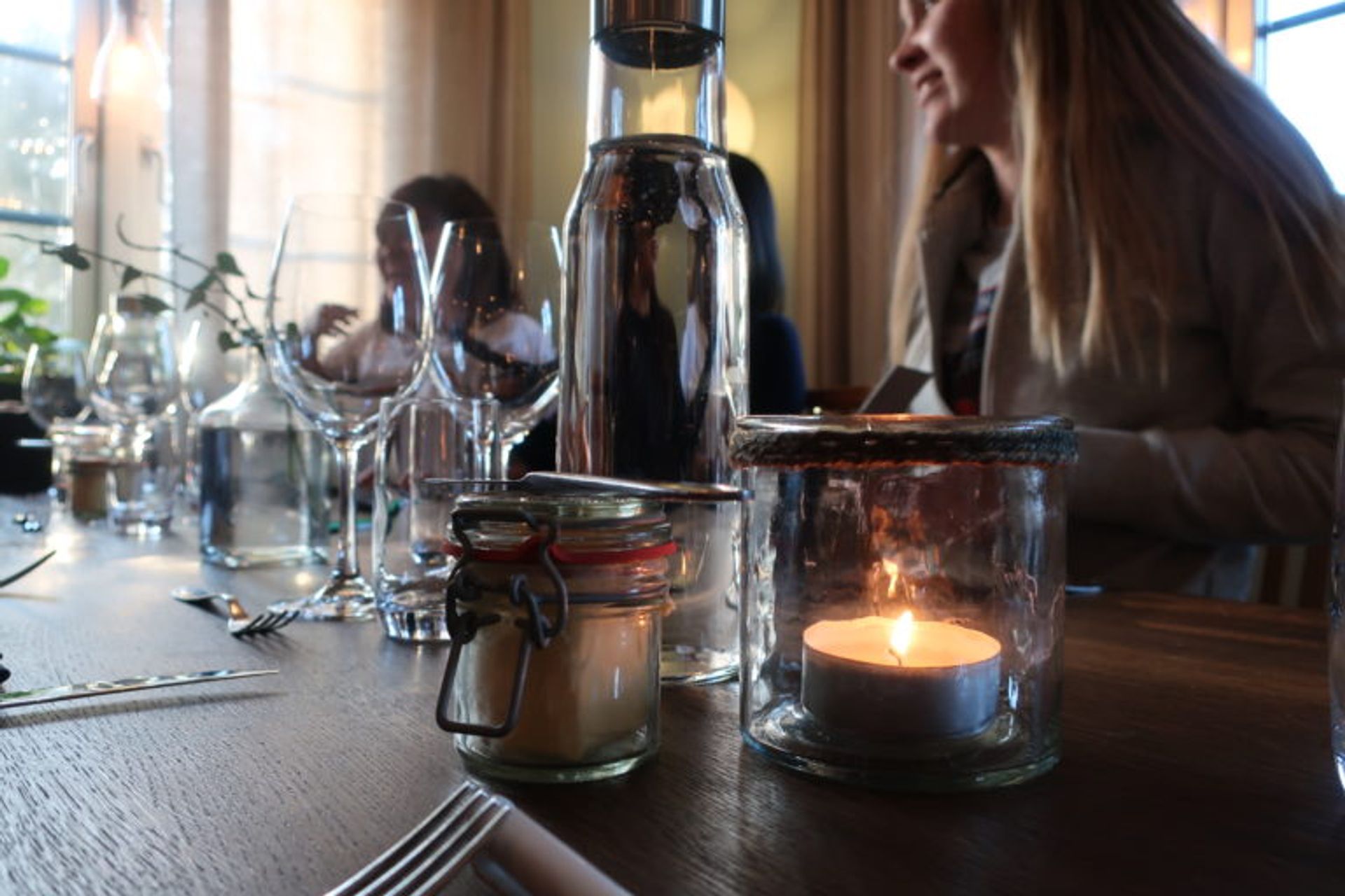 Close up at a set table. It is a candle, a water bottle, cutlery and a flower further back.