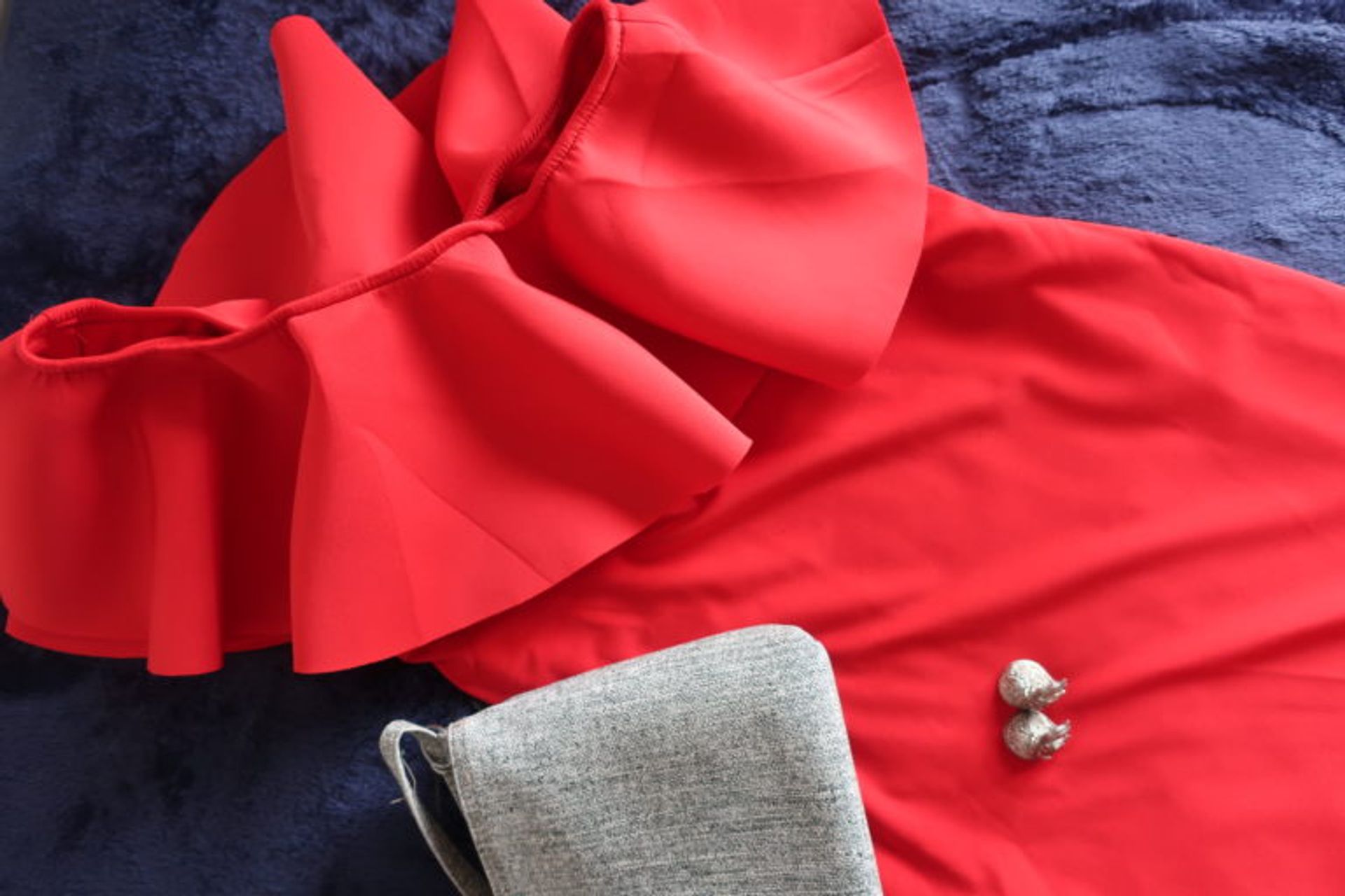 A red dress, grey bag, and earrings laid out on a bed. 