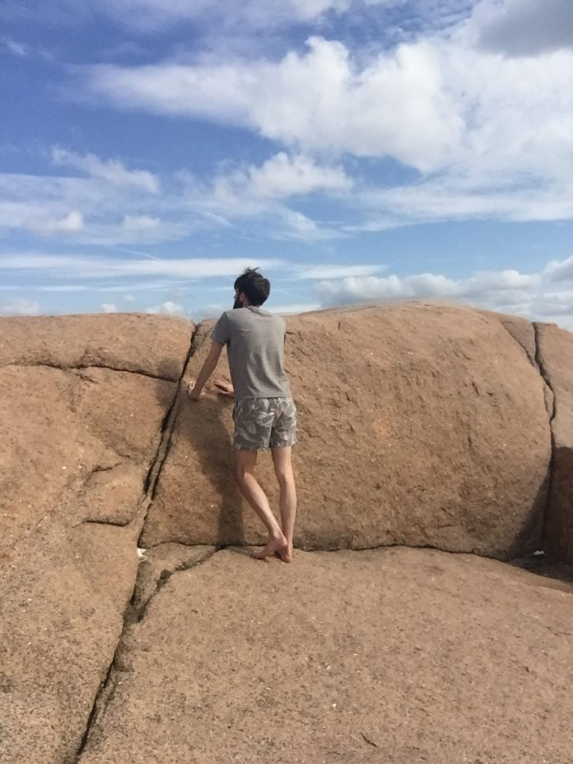 A man leaning on a red rock of the western archipelago. The sky is blue but a bit cloudy.