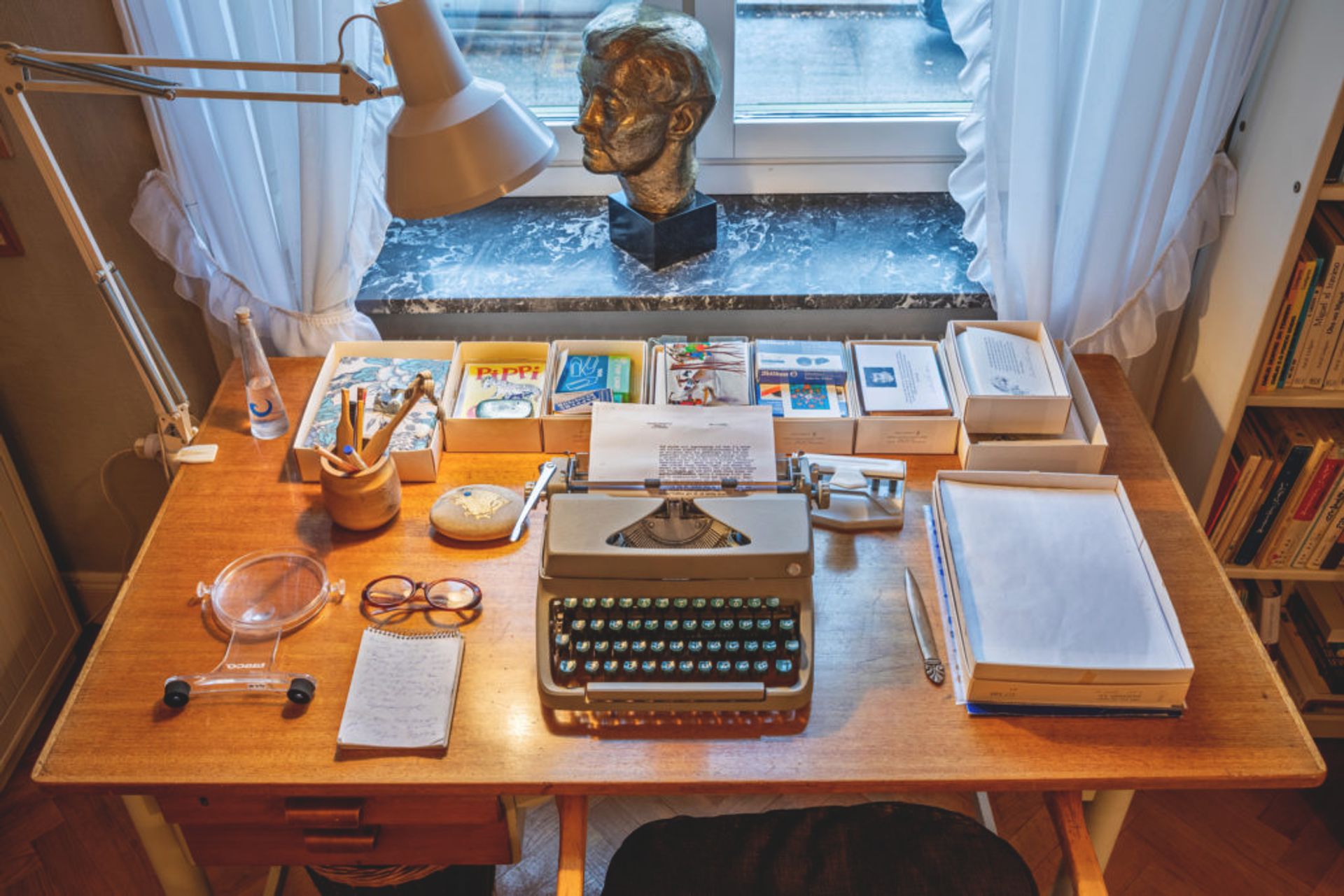 Close-up of a table with a typewriter, paper, pens and notebooks on it.