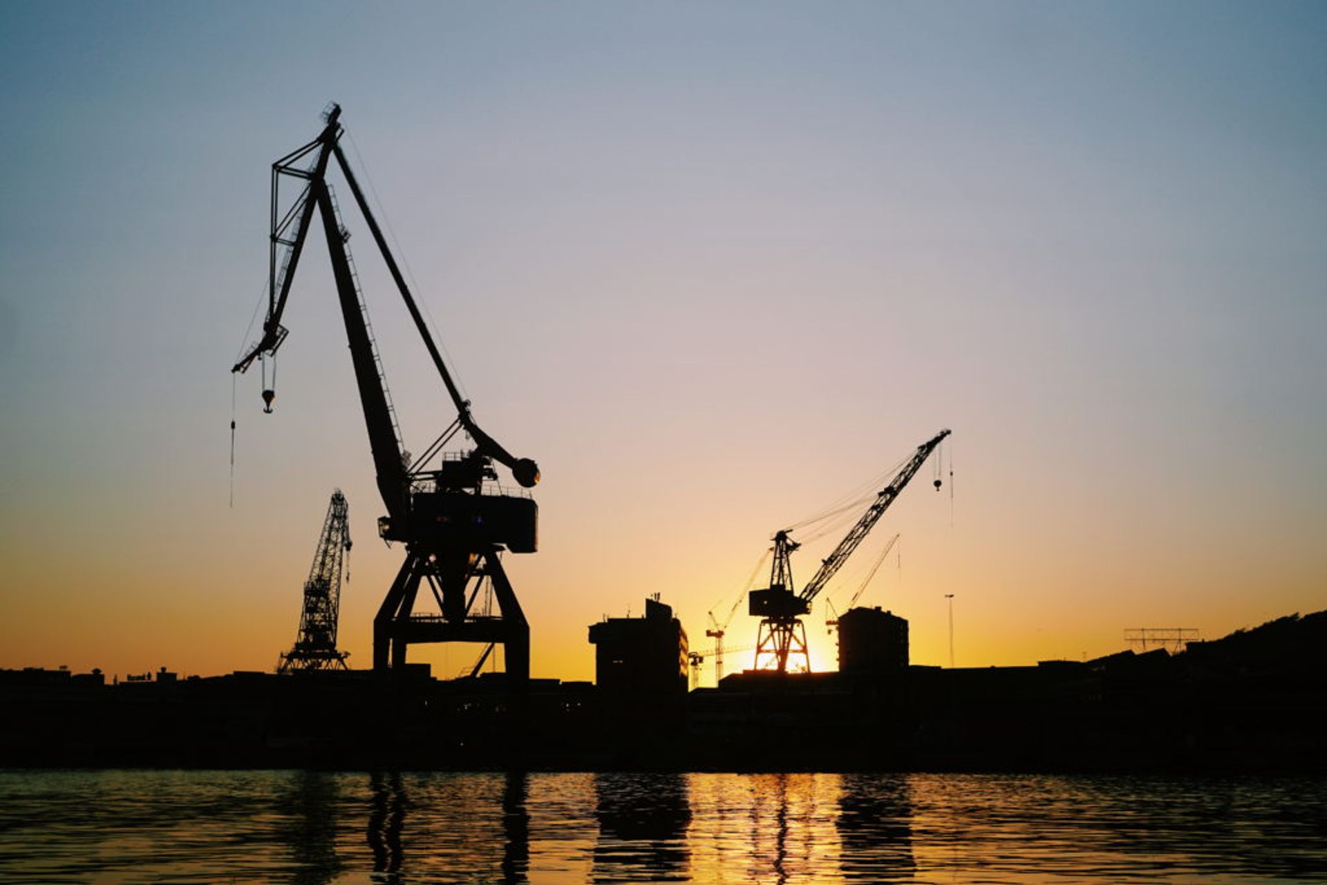 Building cranes silhouetted by a sunset.