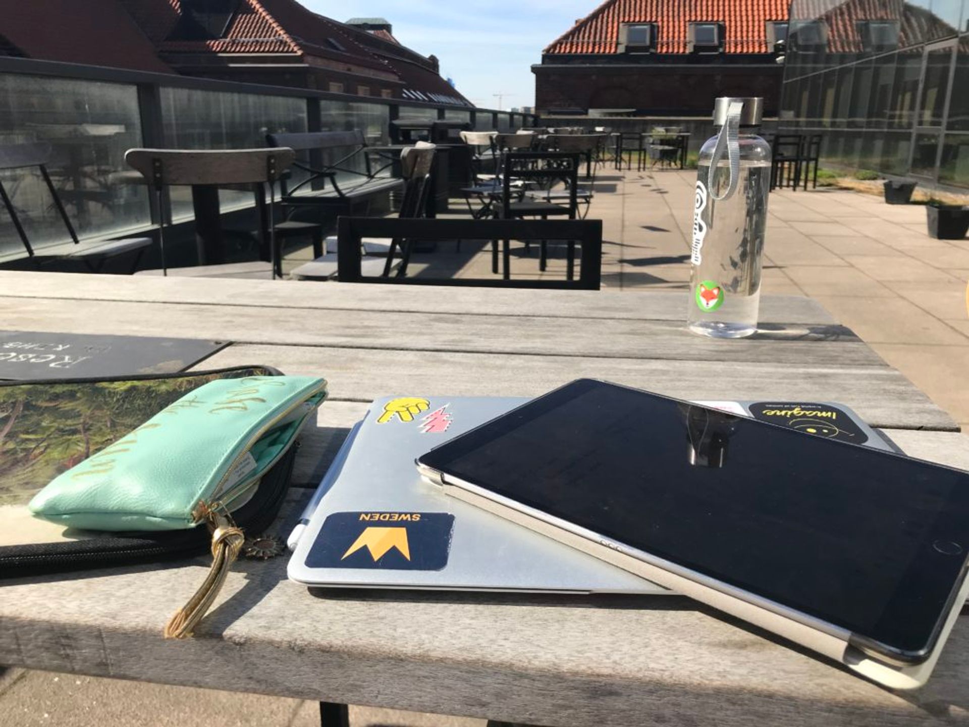 Laptop, notebook and bottle of water on a bench outside.