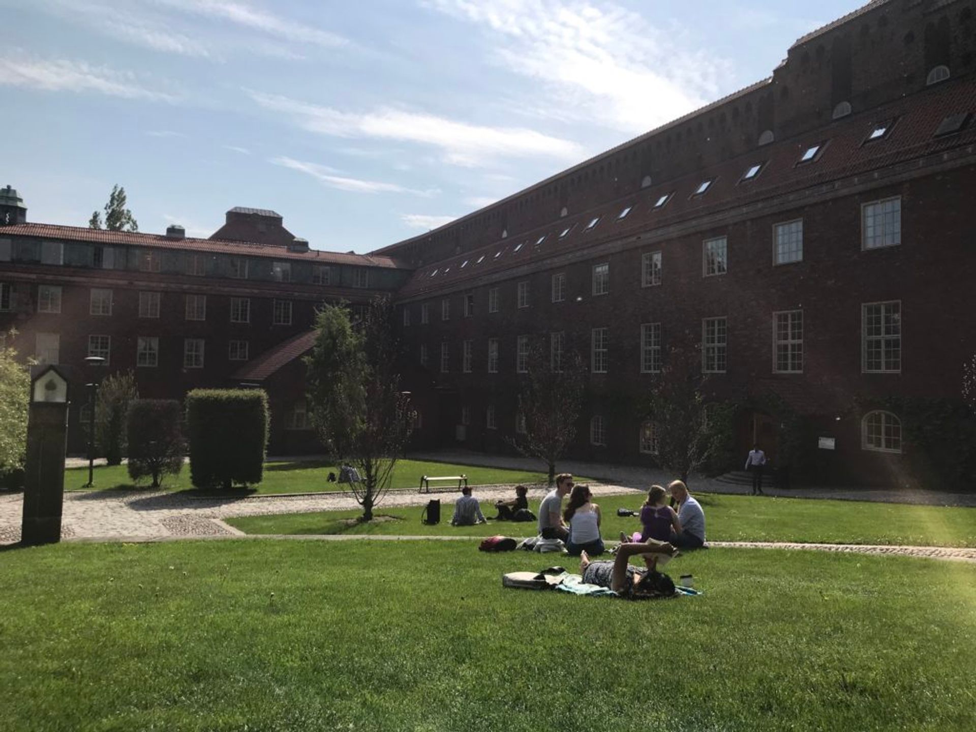 Students sitting and lying on the grass outside a university building.