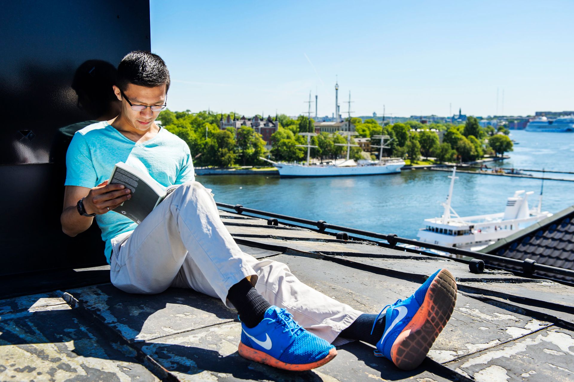 Man sits on a rootop reading a book.