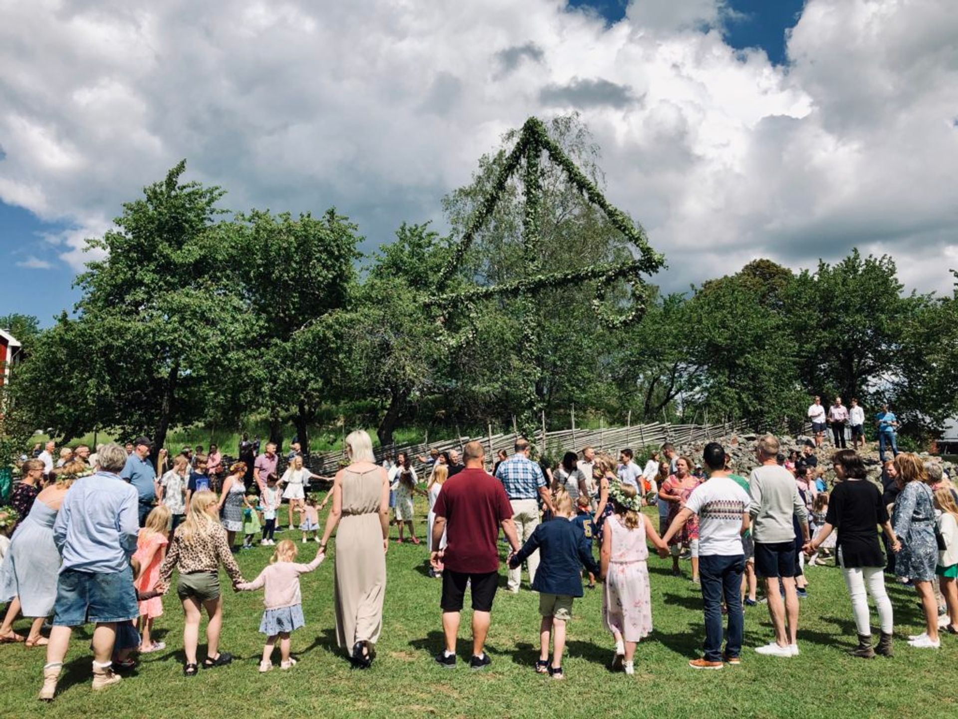 People of all ages holding hands and dancing around a maypole.