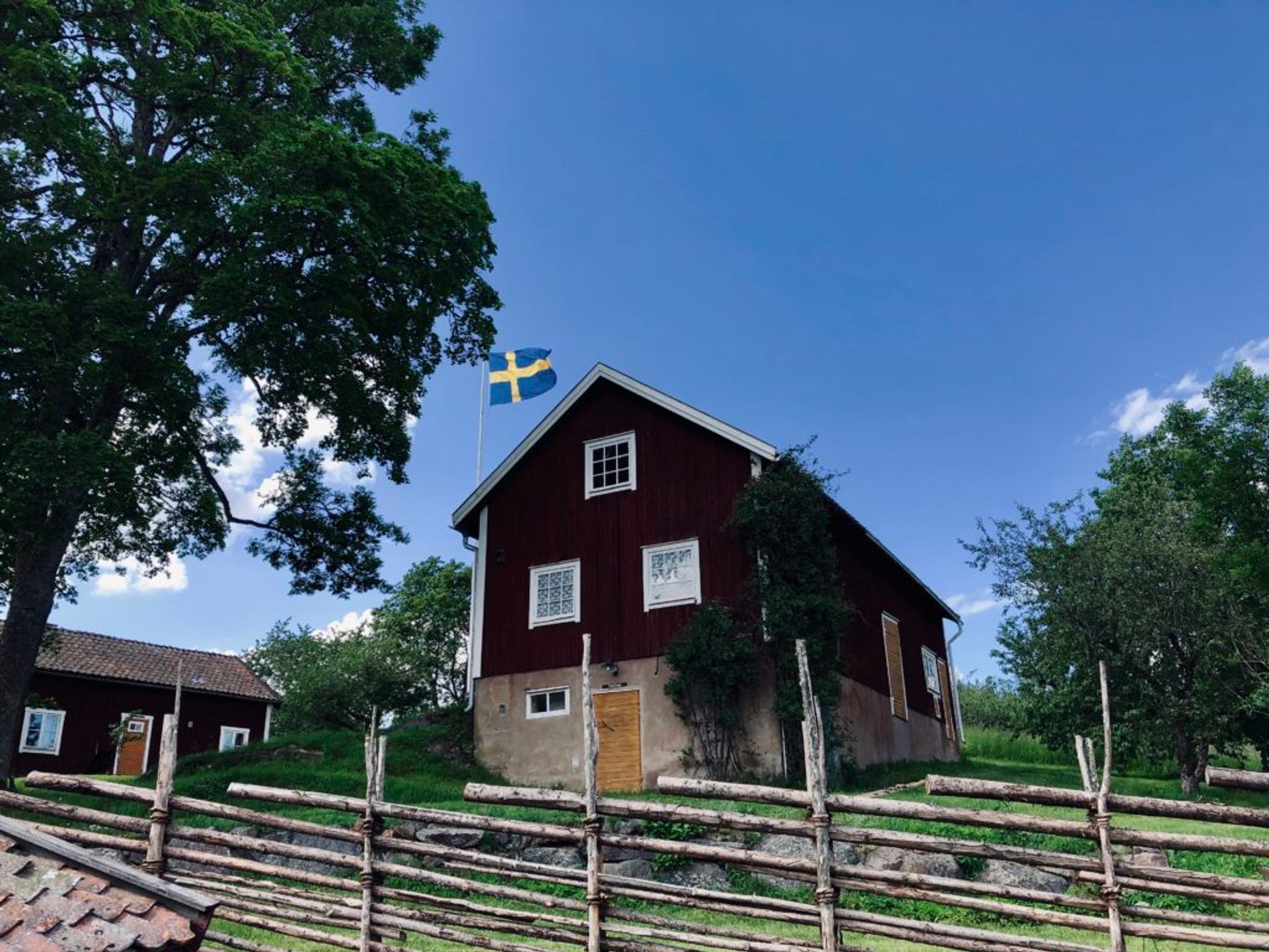 A Swedish flag flying beside a red, wooden building.