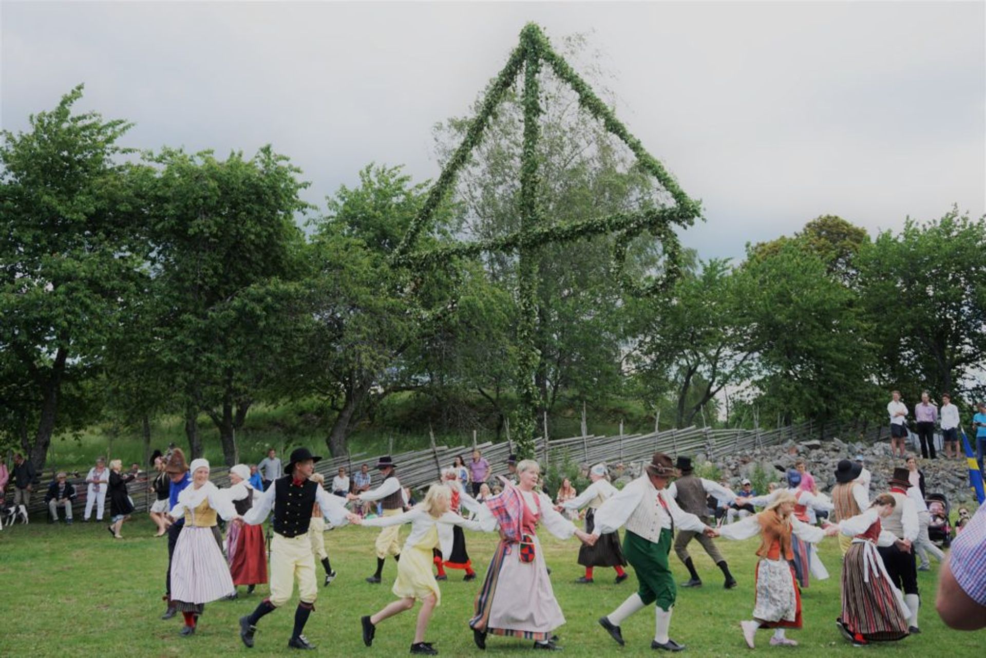 People dressed in traditional folk costumes dancing around a maypole.
