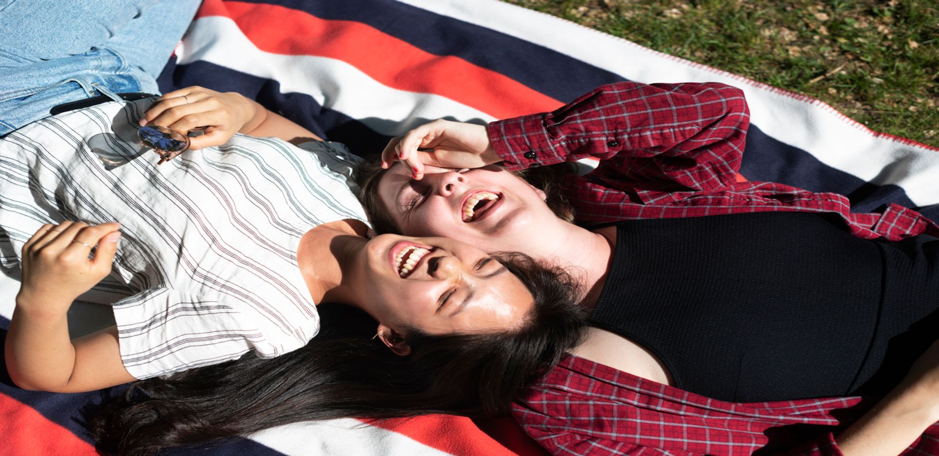 Two students lying on a picnic blanket and laughing.