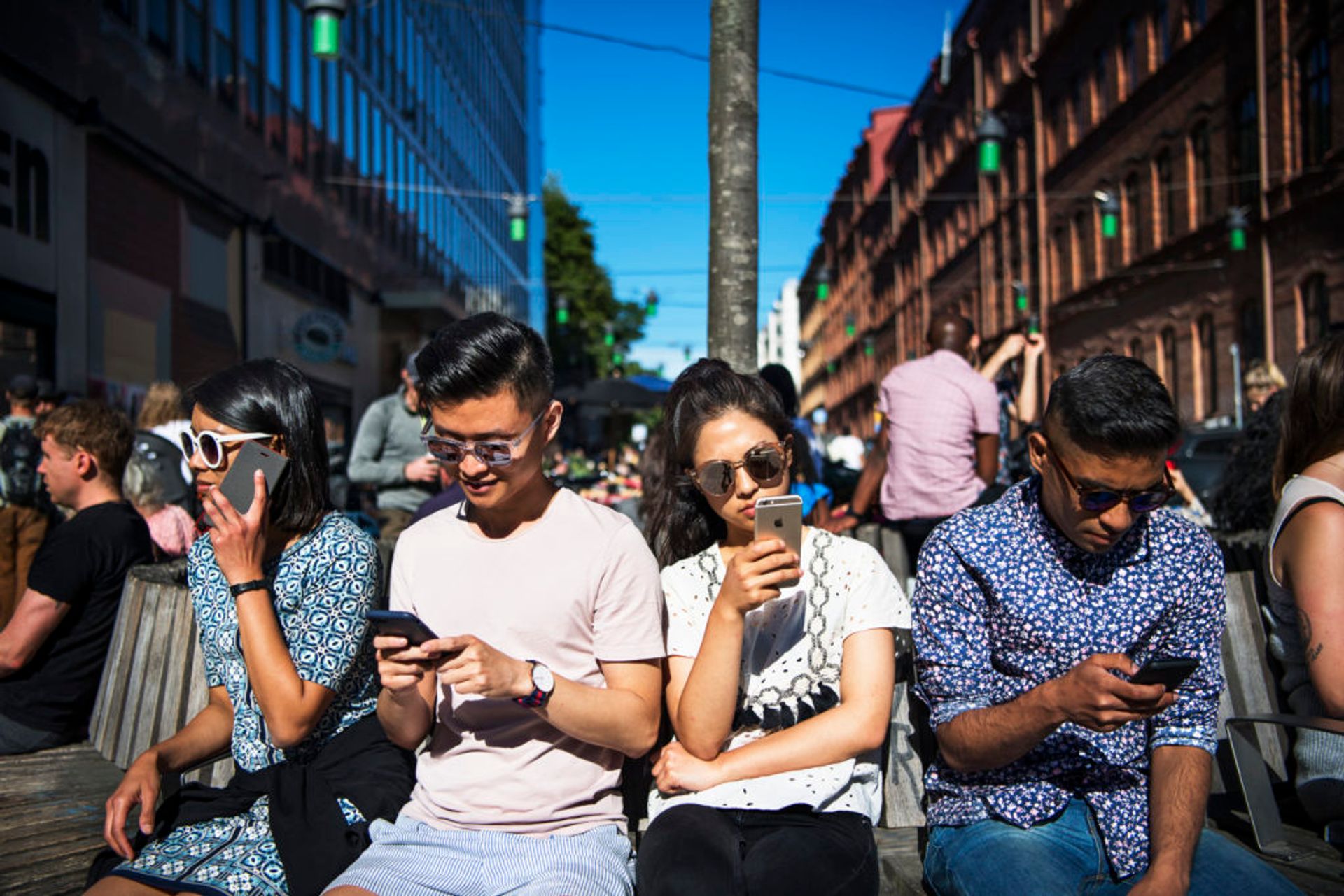 Four students sit together in a line, all looking at their mobile phones.