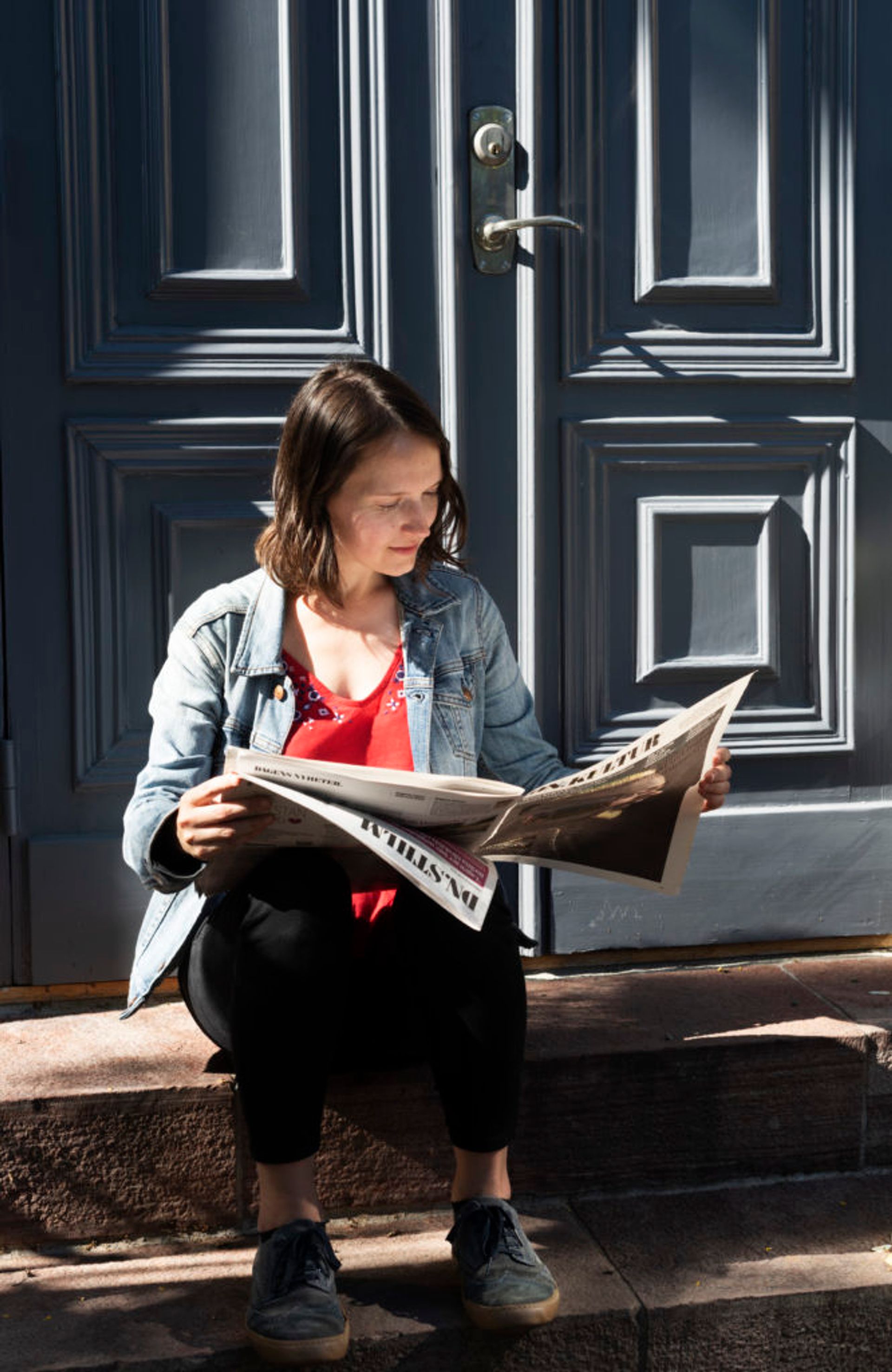 A student sitting on doorstep, reading a newspaper.