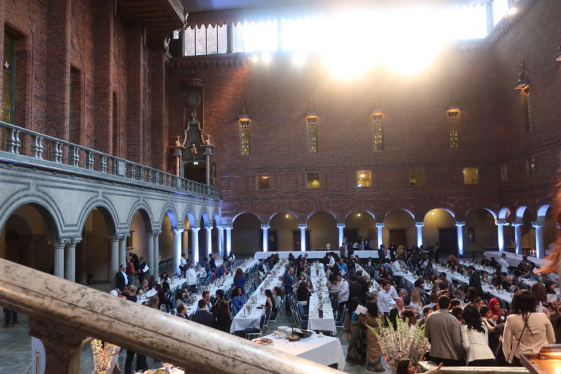 Hundreds of people sitting at long tables in a large hall.