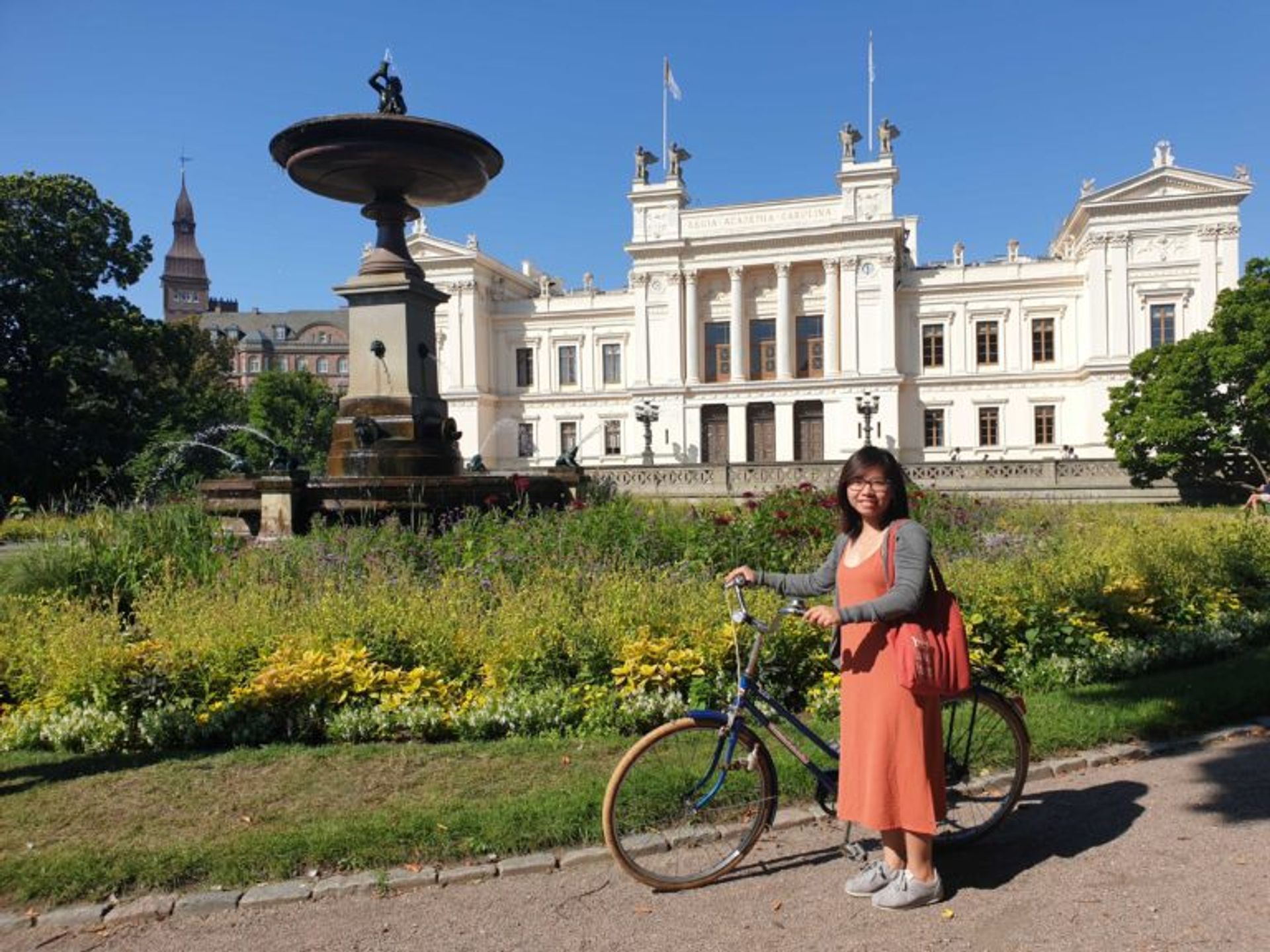 Student standing with a bicycle in front of a white building.