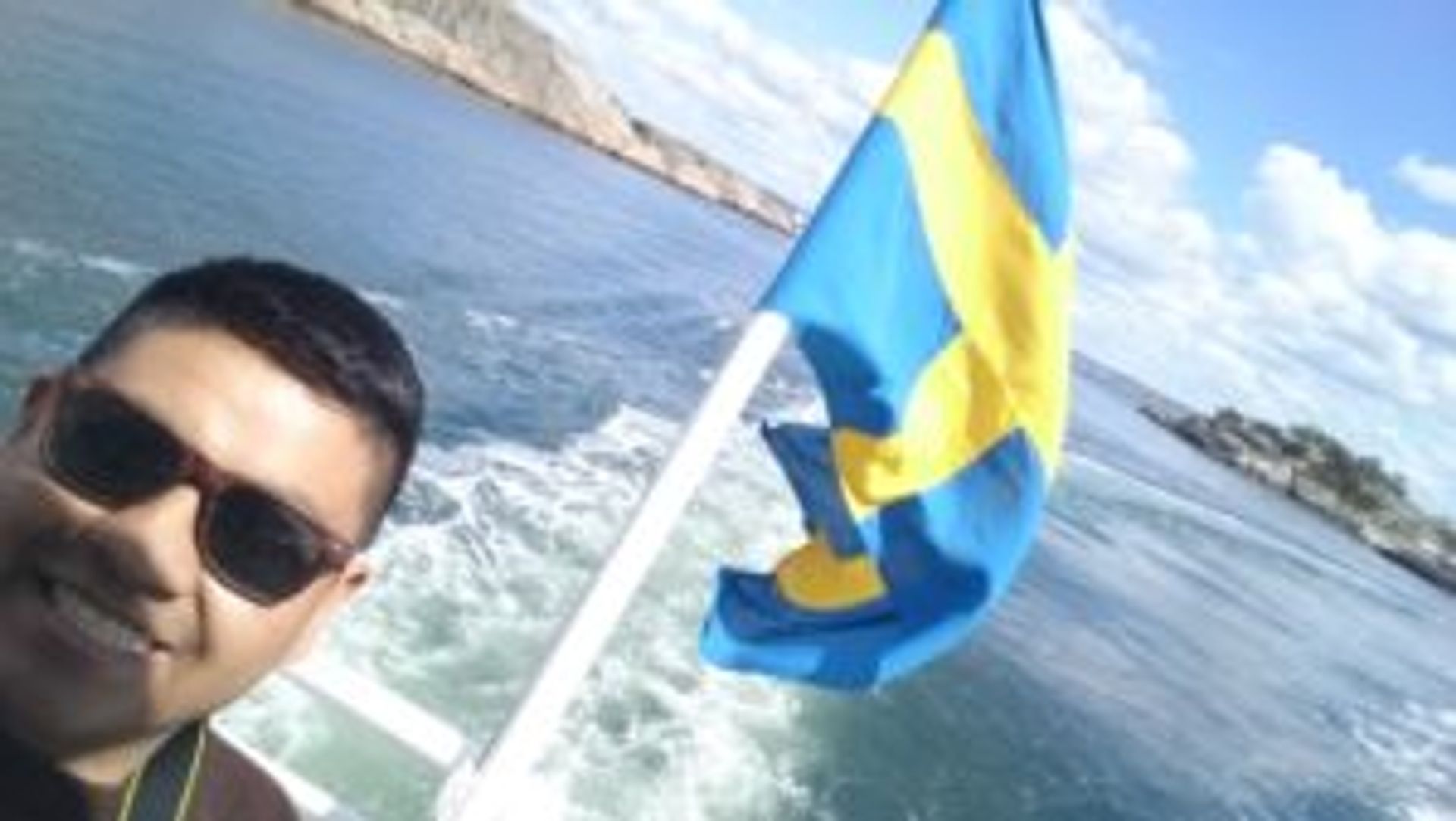 Student on a boat standing beside a Swedish flag.