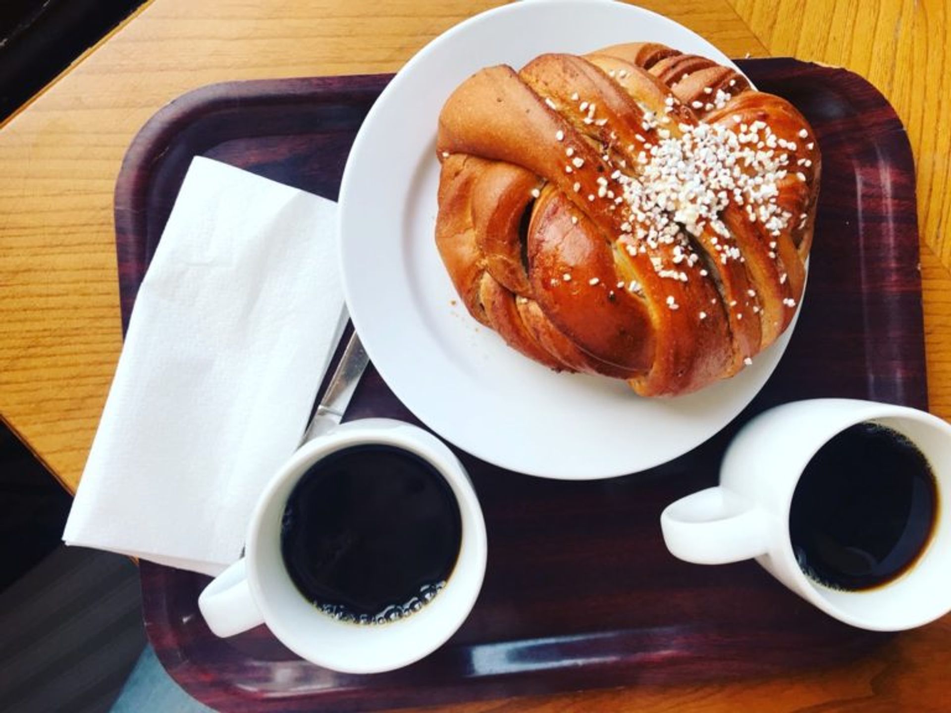 Two cups of black coffee and a cinnamon bun on a tray.
