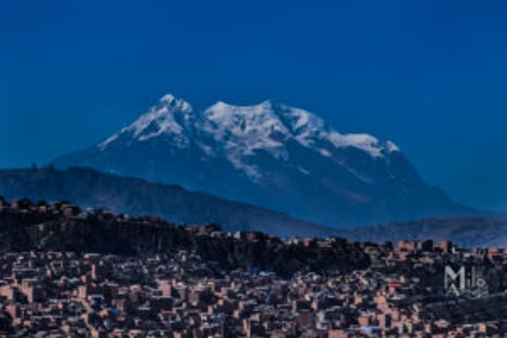 A snow-covered mountain above a large city.