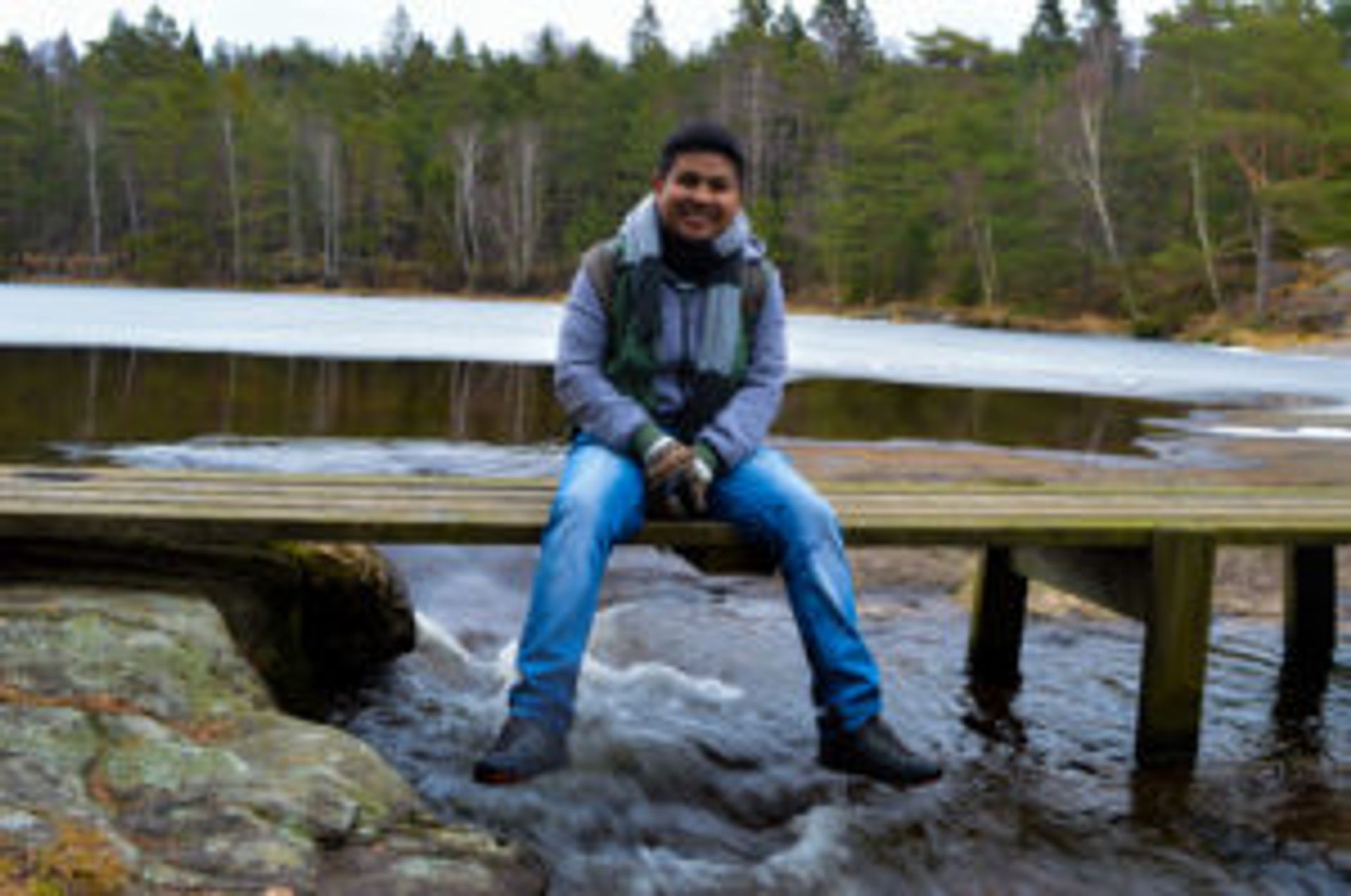 Camilo sitting on a small, wooden footbridge by a lake outside of Gothenburg.