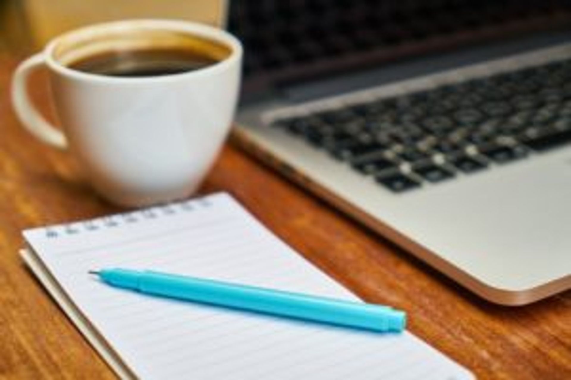 Close-up of a notepad and pen beside a laptop.