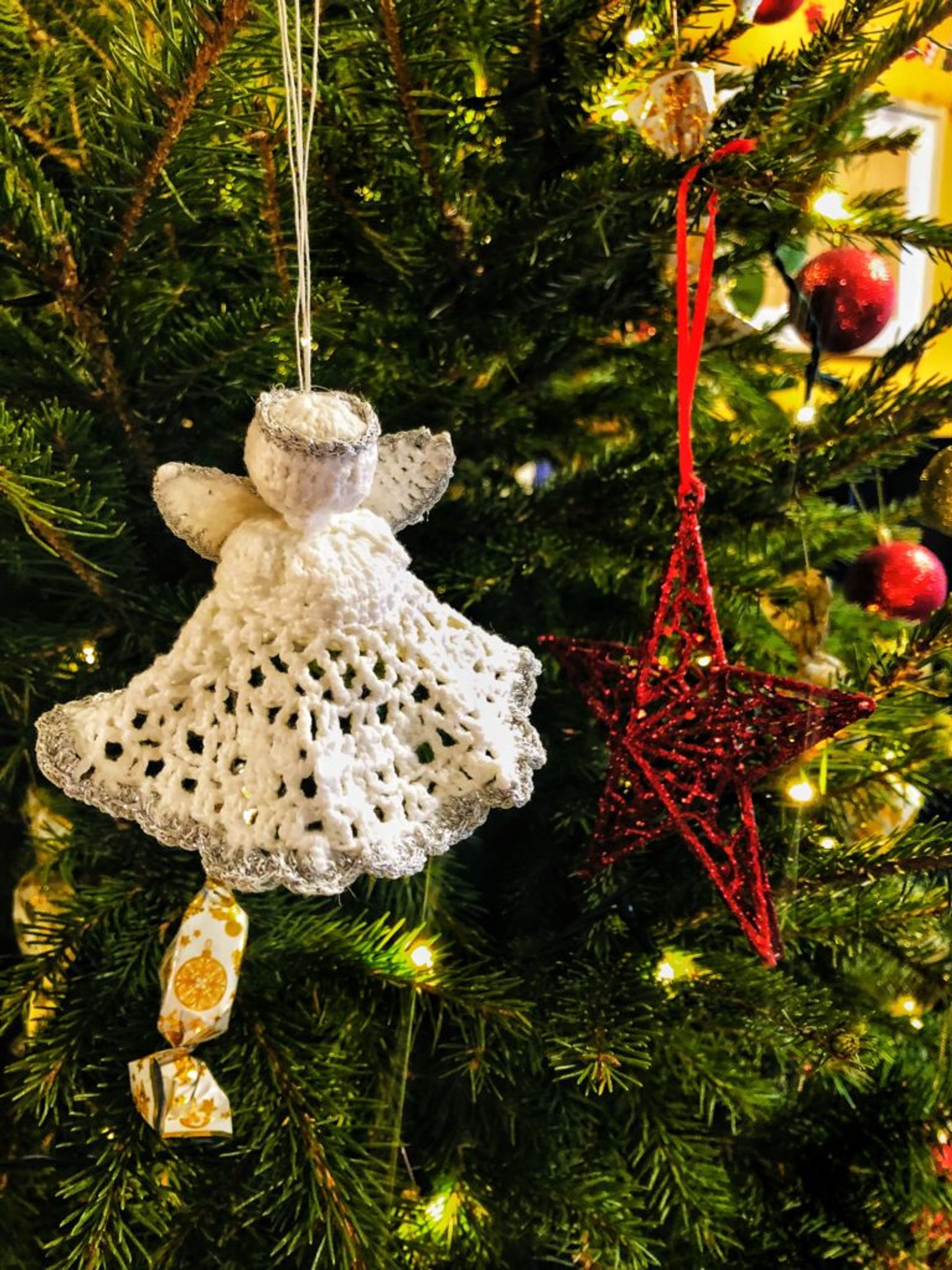 A crochet angel decoration hanging on a Christmas tree.